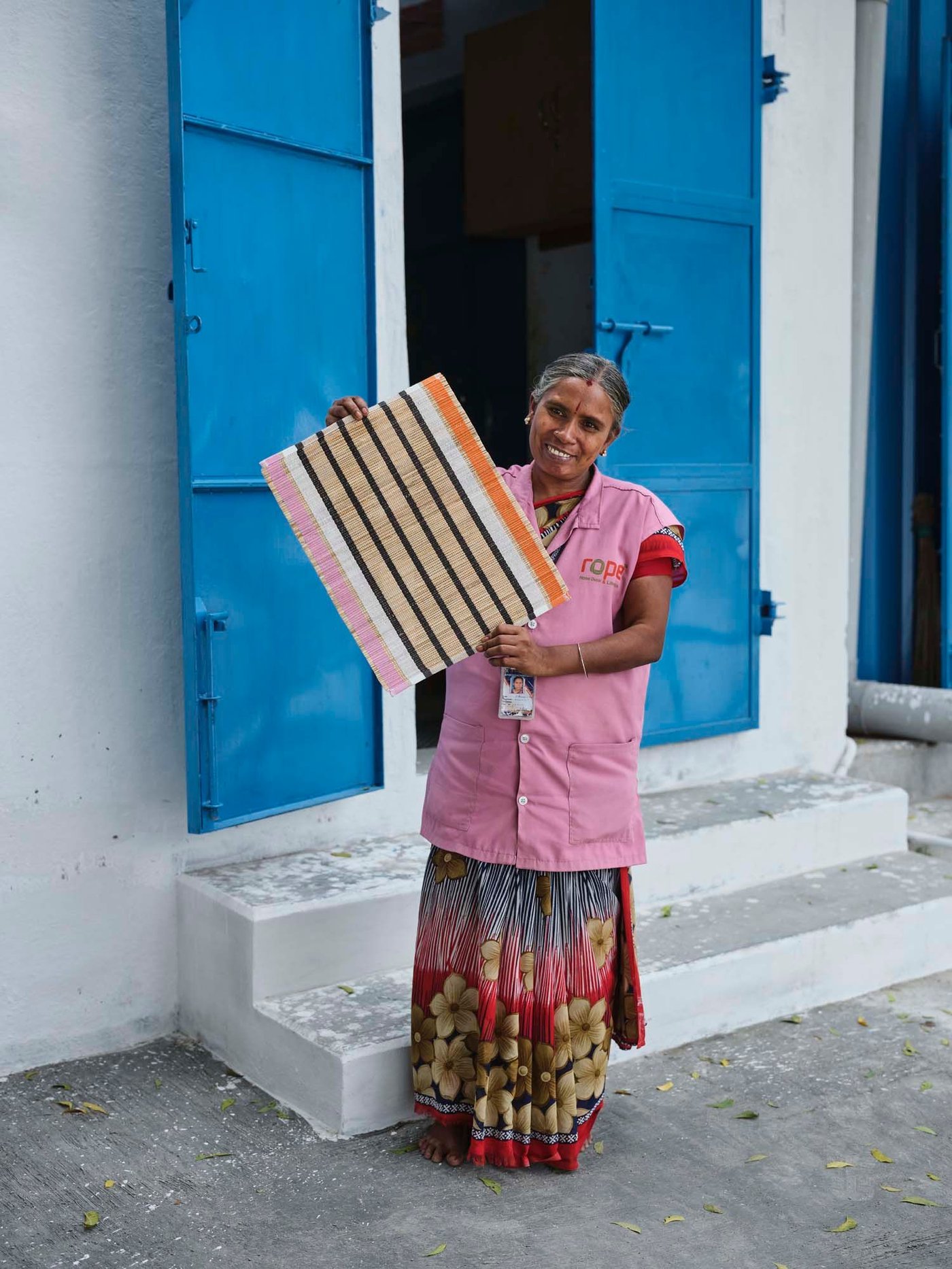 A person stands holding a woven place mat in front of open blue doors.