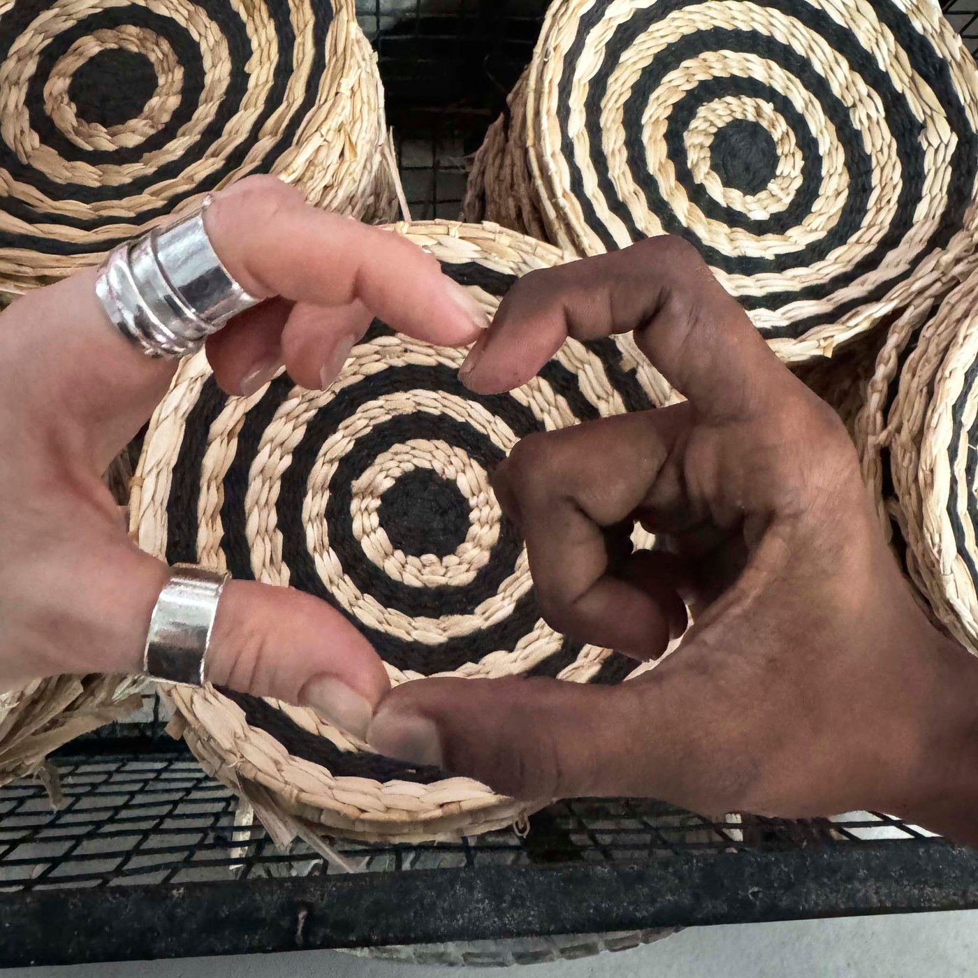Two separate hands join together to create a heart, in front of woven baskets.
