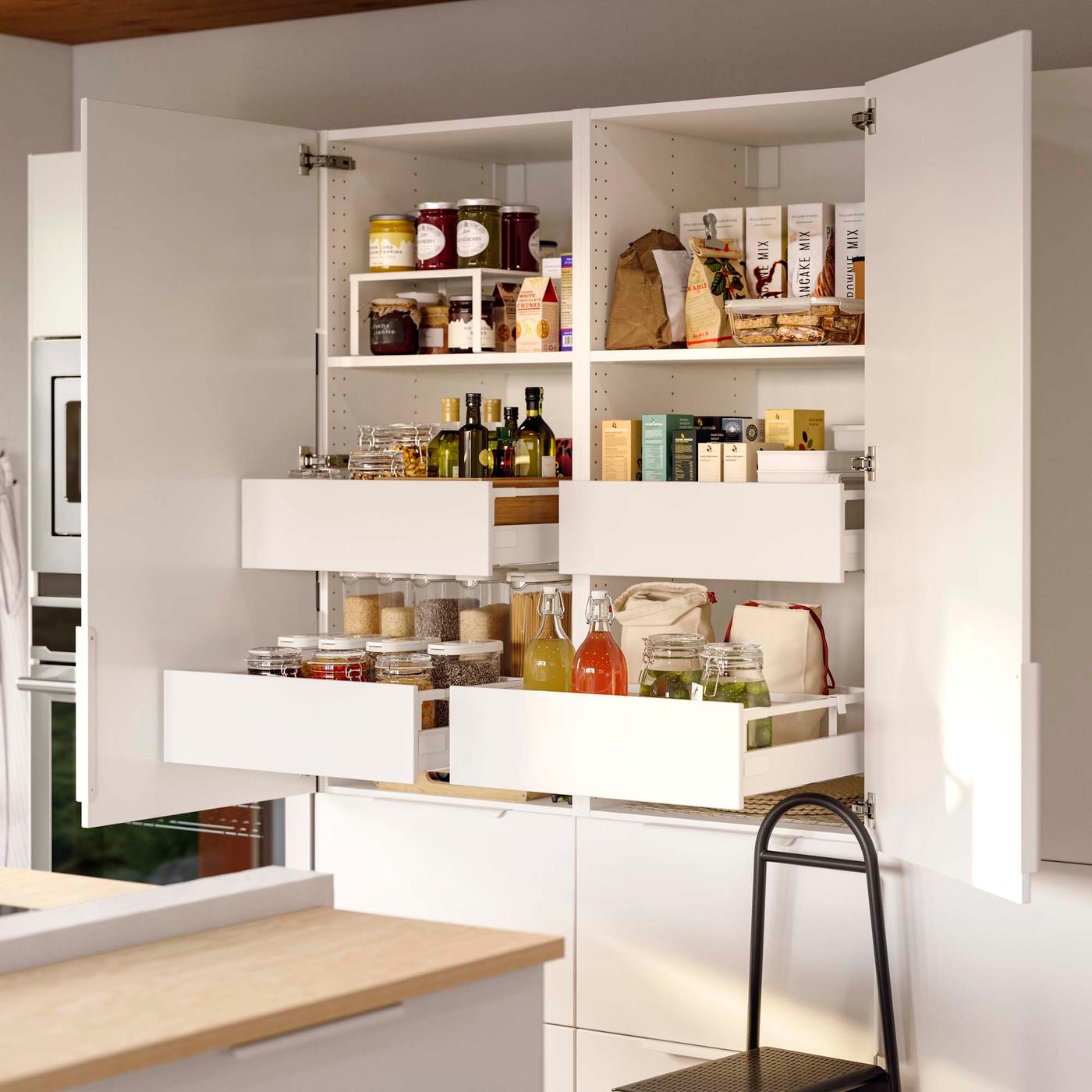Neatly organised food on shelves and in open drawers in two white kitchen cupboards that are side by side. 