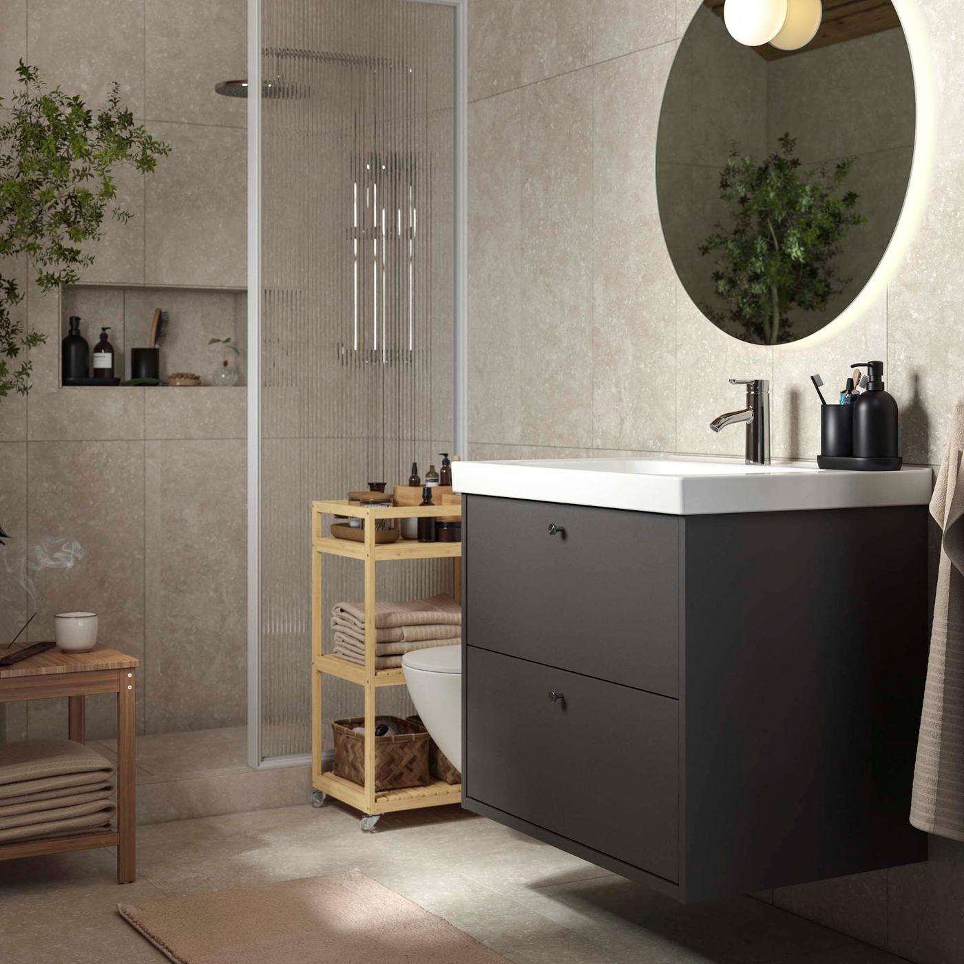 A black under sink cabinet in front of a shower in a beige bathroom. 
