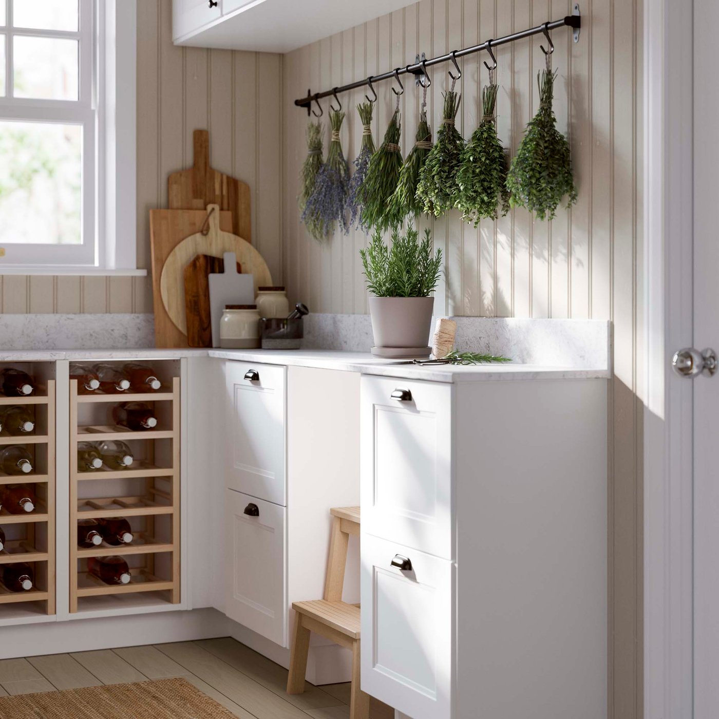 The corner of a white rustic style kitchen with a hanging rail on the wall. Herbs hang out to dry on the rail.