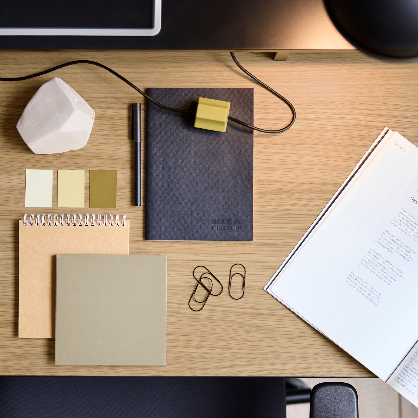 An aerial view of a wood desktop with notebooks, sticky notes and paper clips neatly organised.