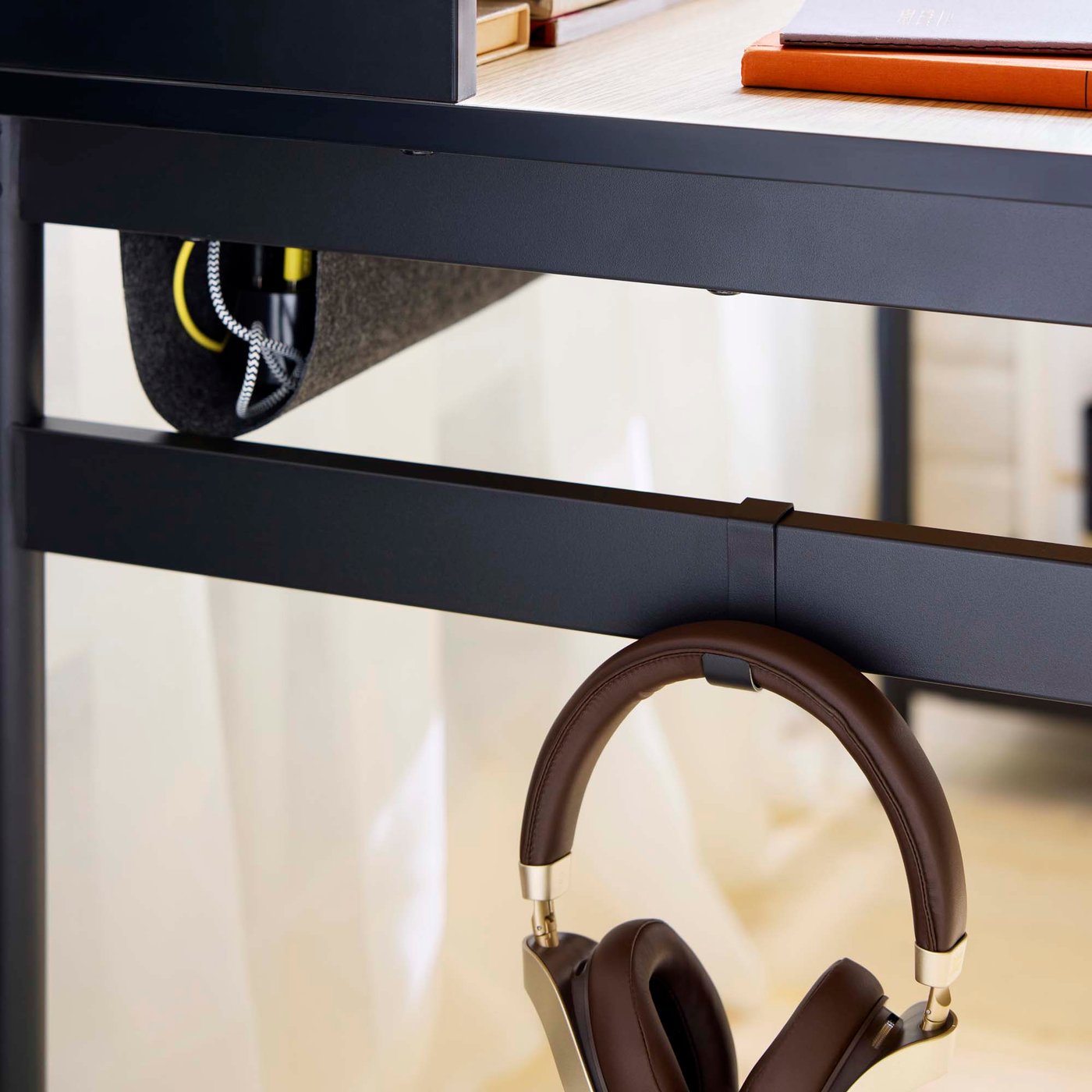 Headphones hang from a hook on a black desk frame.