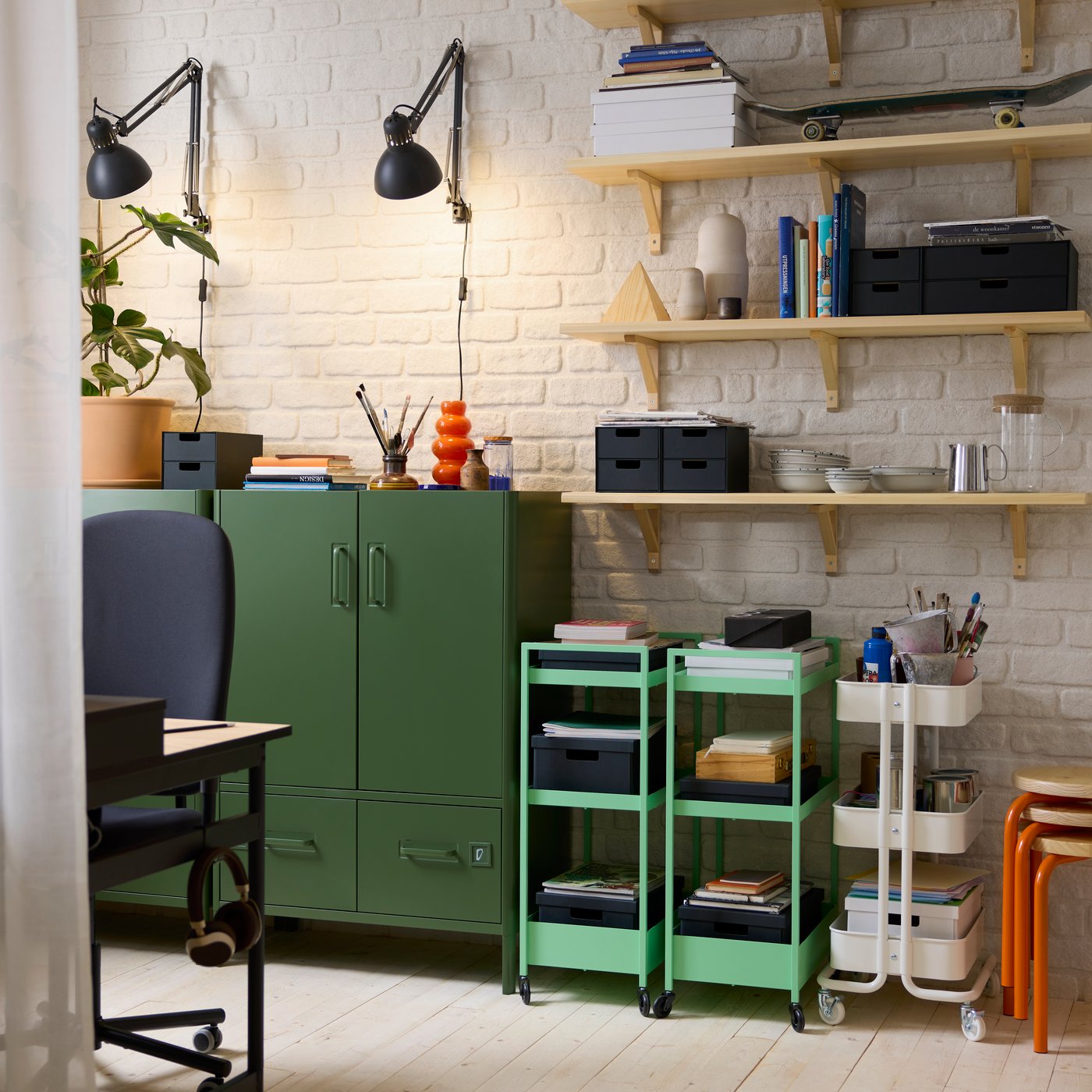 A white brick wall in an industrial style home office. The wall is lined with colourful storage cabinets and trolleys filled with stationery.