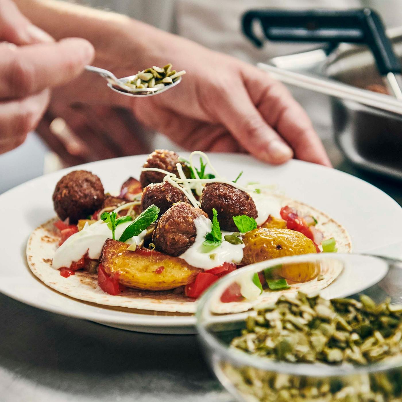 A person adding final touches to a dish of plant-based balls with crispy potato pancakes.