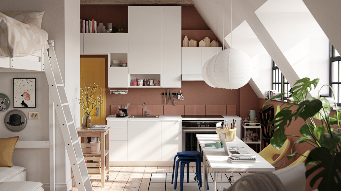 An open plan studio space with a sloped ceiling and a white kitchen in the background.