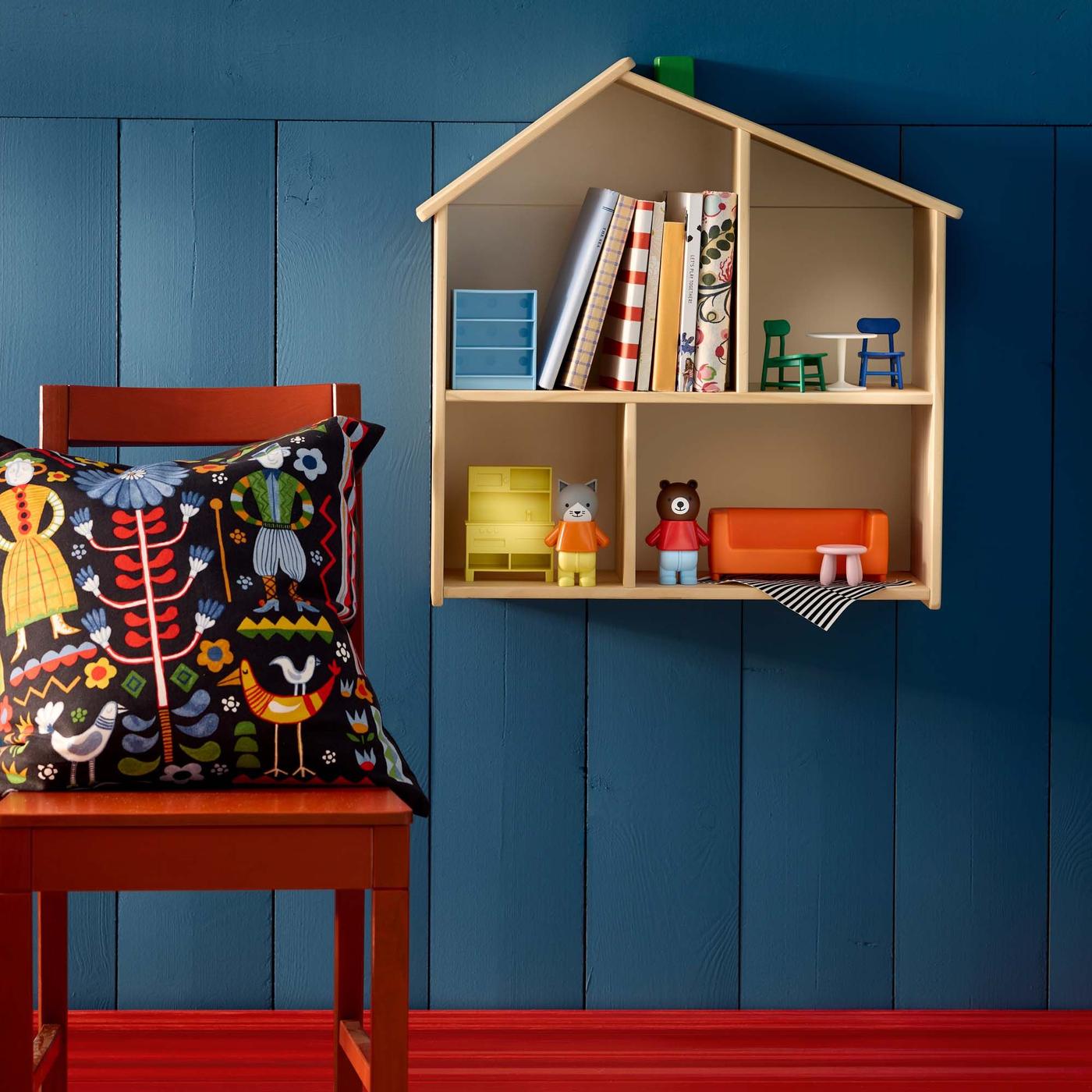 A wood doll house-bookshelf on a blue wall, next to a red stool.