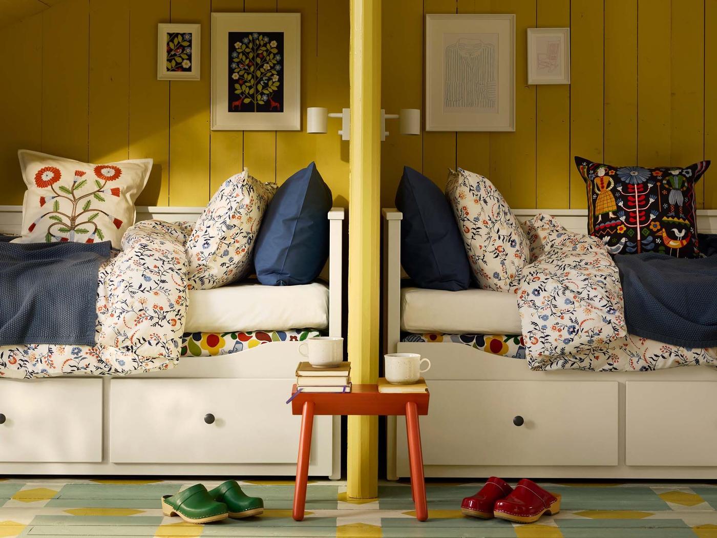 Two HEMNES daybeds are placed side-by-side in a yellow room. Both are decorated with patterned cushions and bedlinen, adding country style inspiration.
