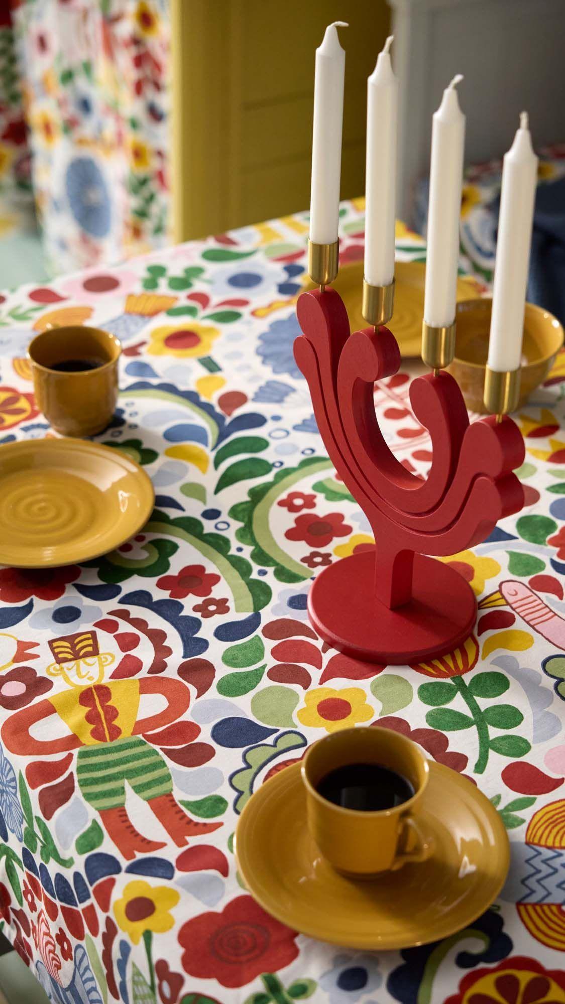 A red VINTERFINT candlestick holder on a colourful floral-patterned tablecloth with yellow dishware and mugs.