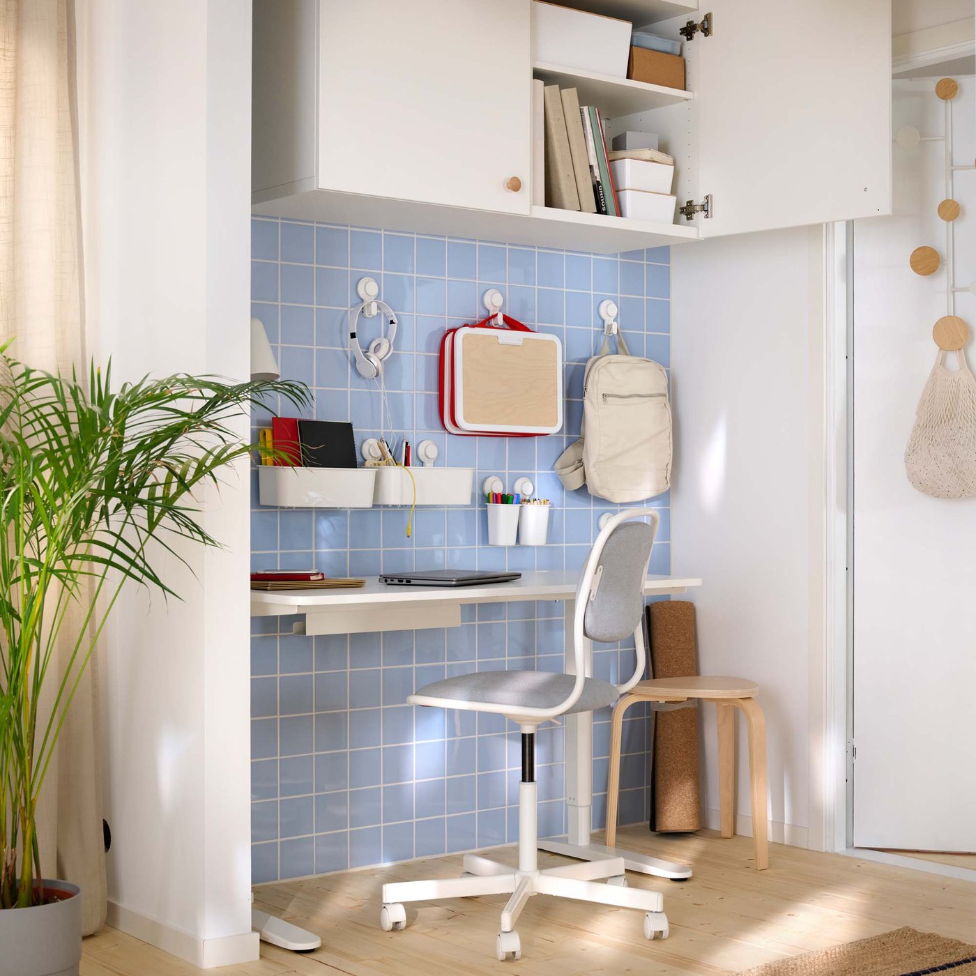 A home office area in the hallway. Bags and accessories hang from hooks above the desk on a blue tiled wall.