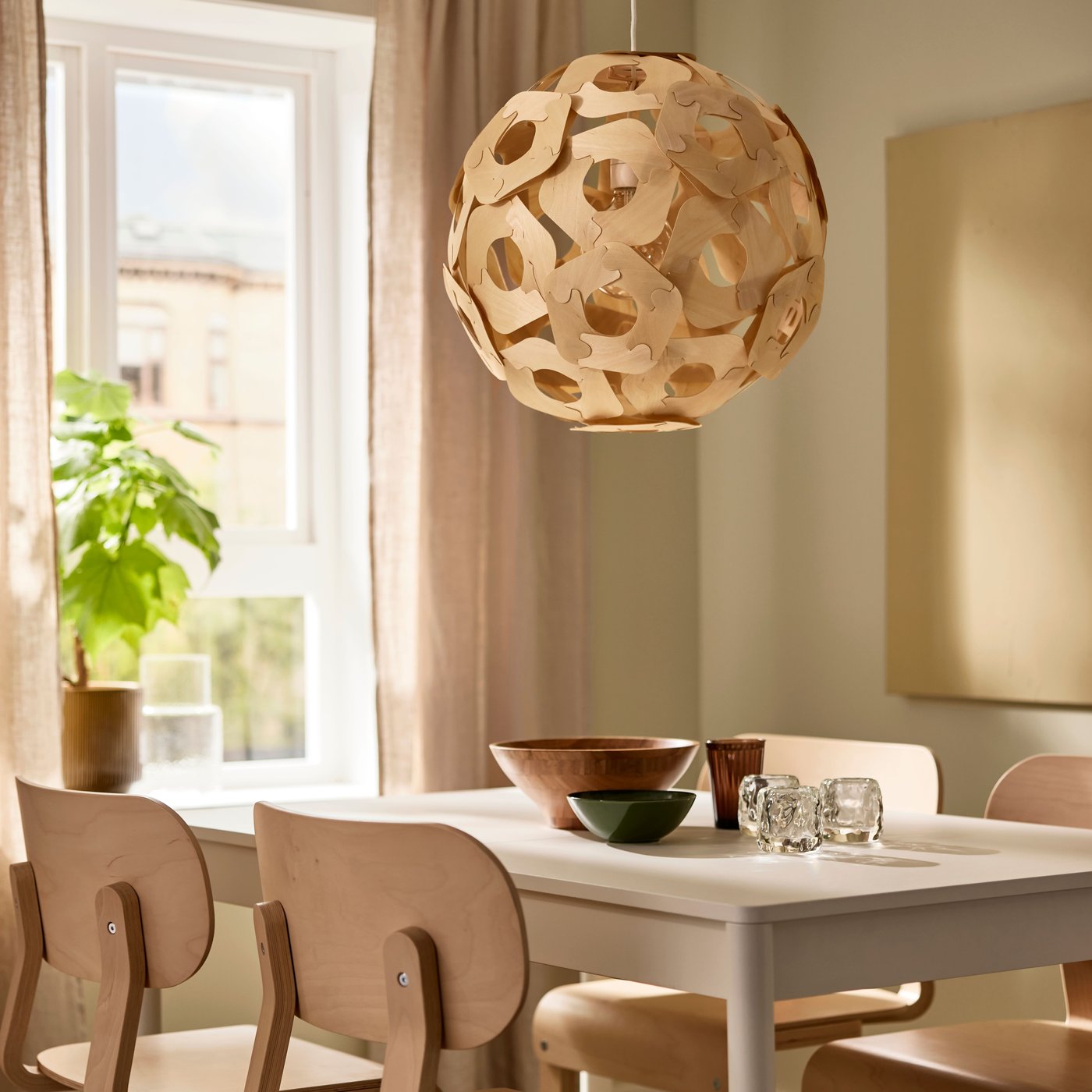A spherical wooden look pendant lamp, hanging near a window with earthy walls and a plant beside.