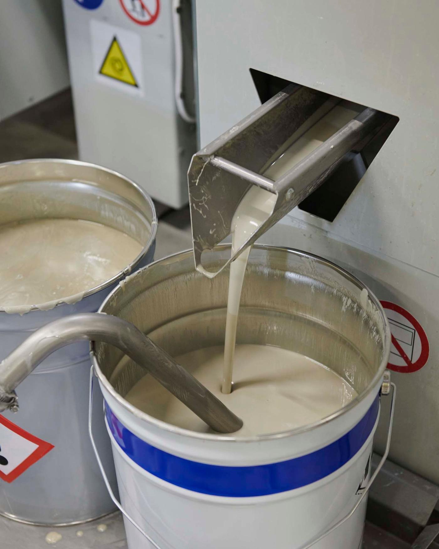 Excess paint pours into a bucket beside the soft-roller machine.