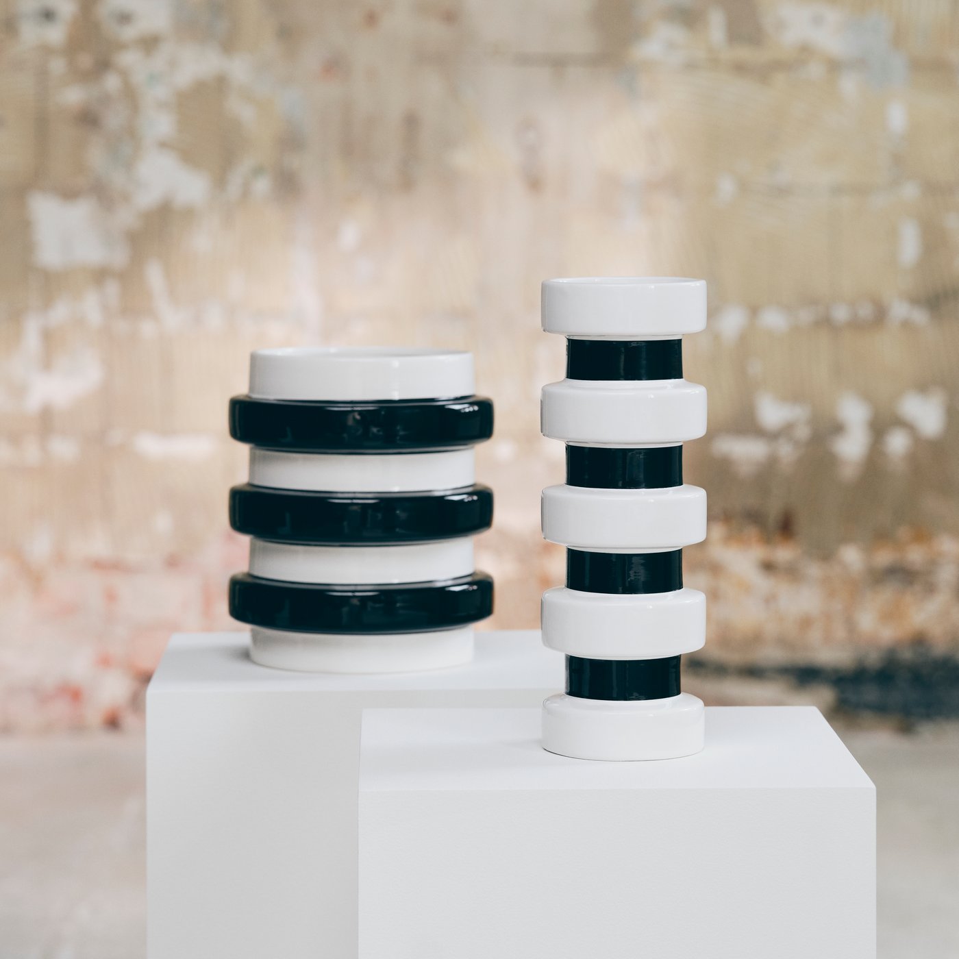 Two black and white sculptural vases displayed on white plinths in an industrial gallery