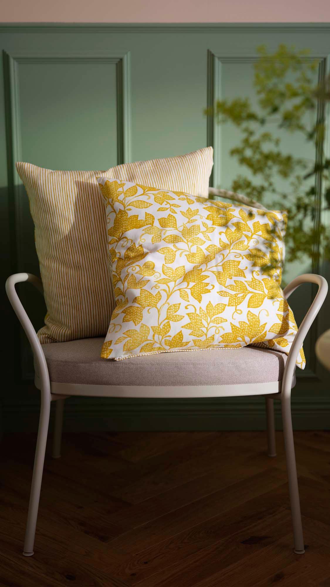 Two cushions on a grey armchair, one striped and one floral, with a green wall in the background.