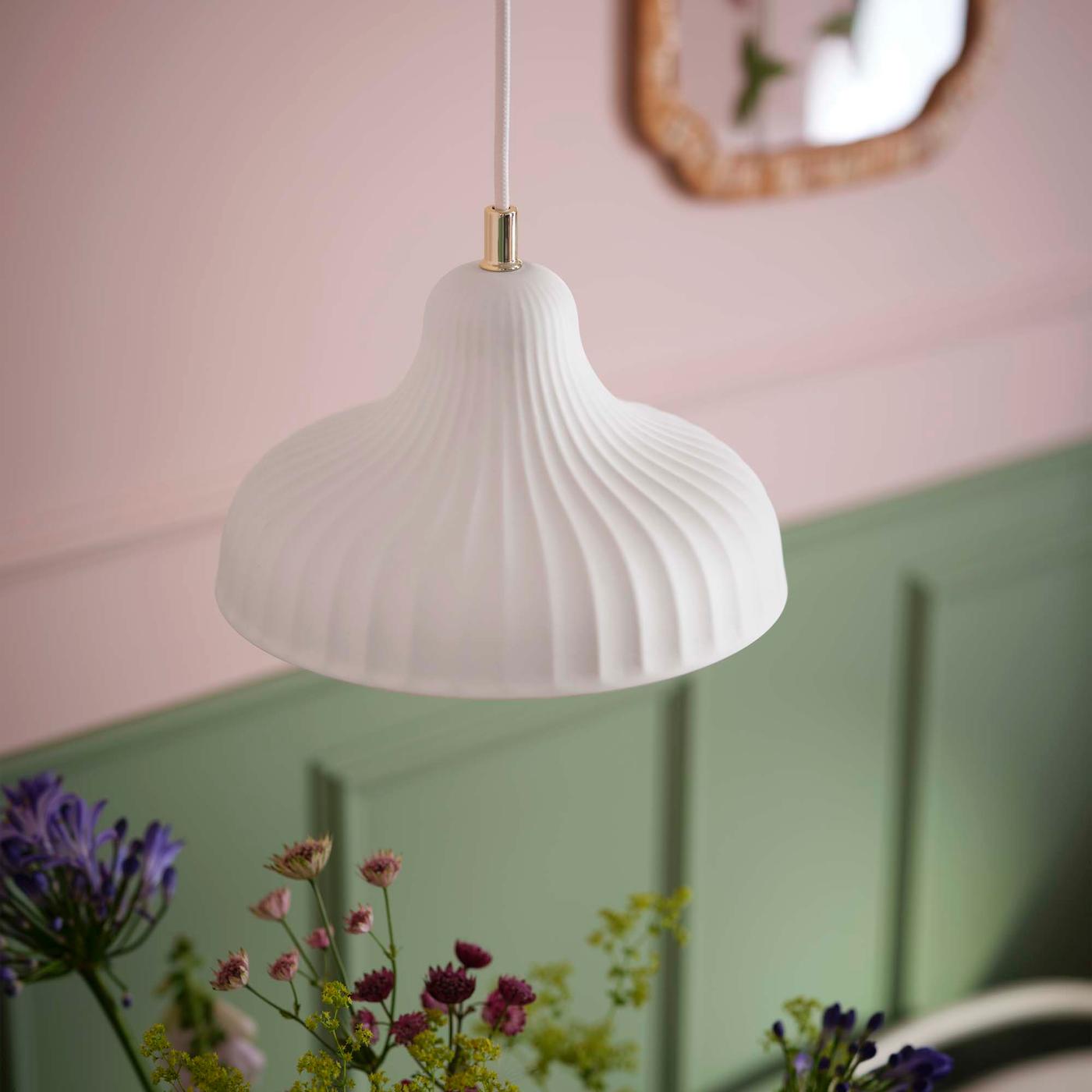 A white ceramic pendant lamp in front of a pink and green wall.