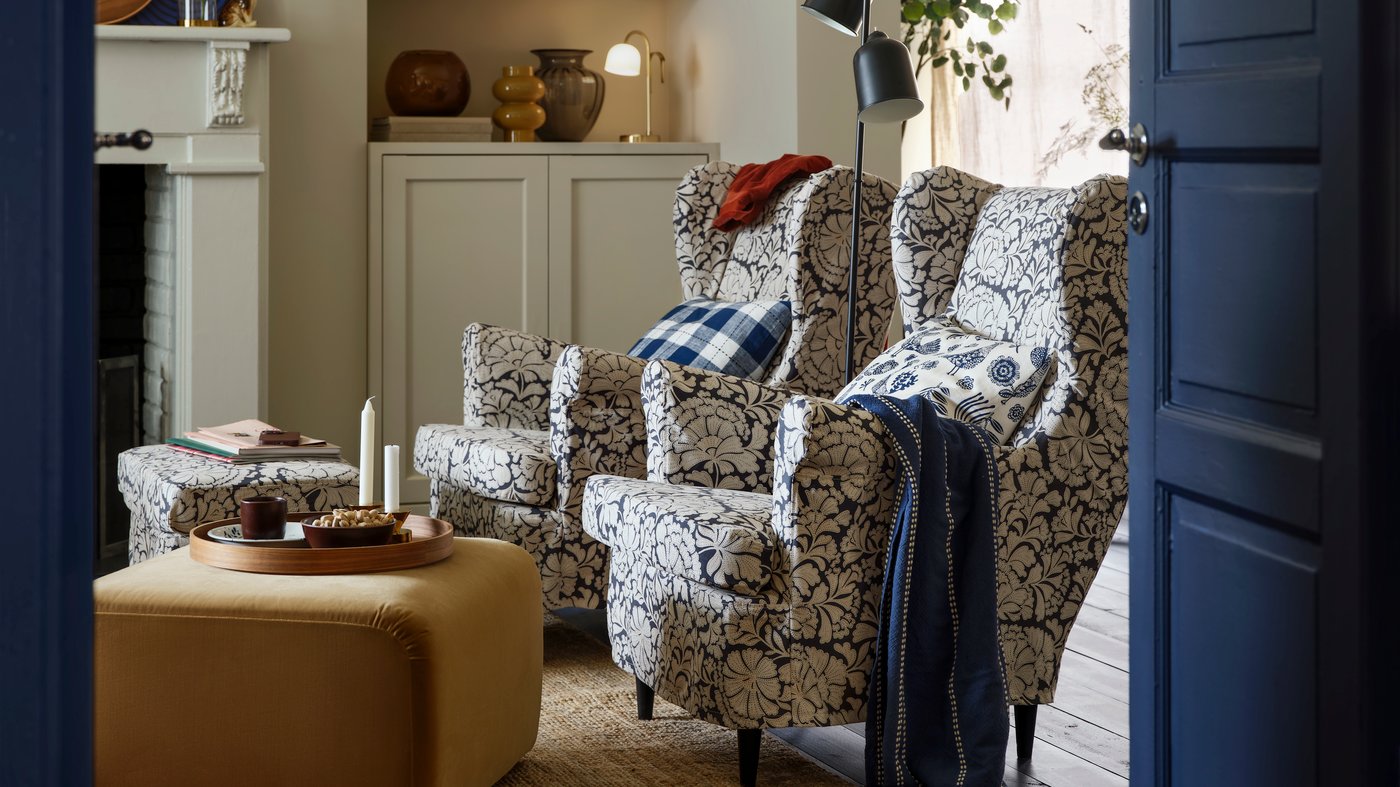 A view through dark blue doors into a living room with a pair of blue and white armchairs with a floral pattern and a yellow pouffe.