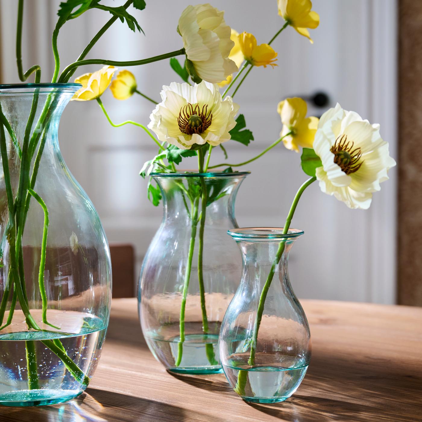 A trio of BERGKÖRSBAR glass vases in varying heights with yellow flowers.