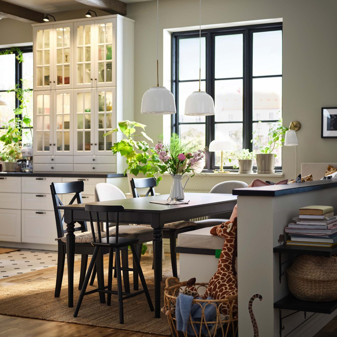 The dining area of a black and white rustic style kitchen. Plants and vases sit on the dining table and windowsills.