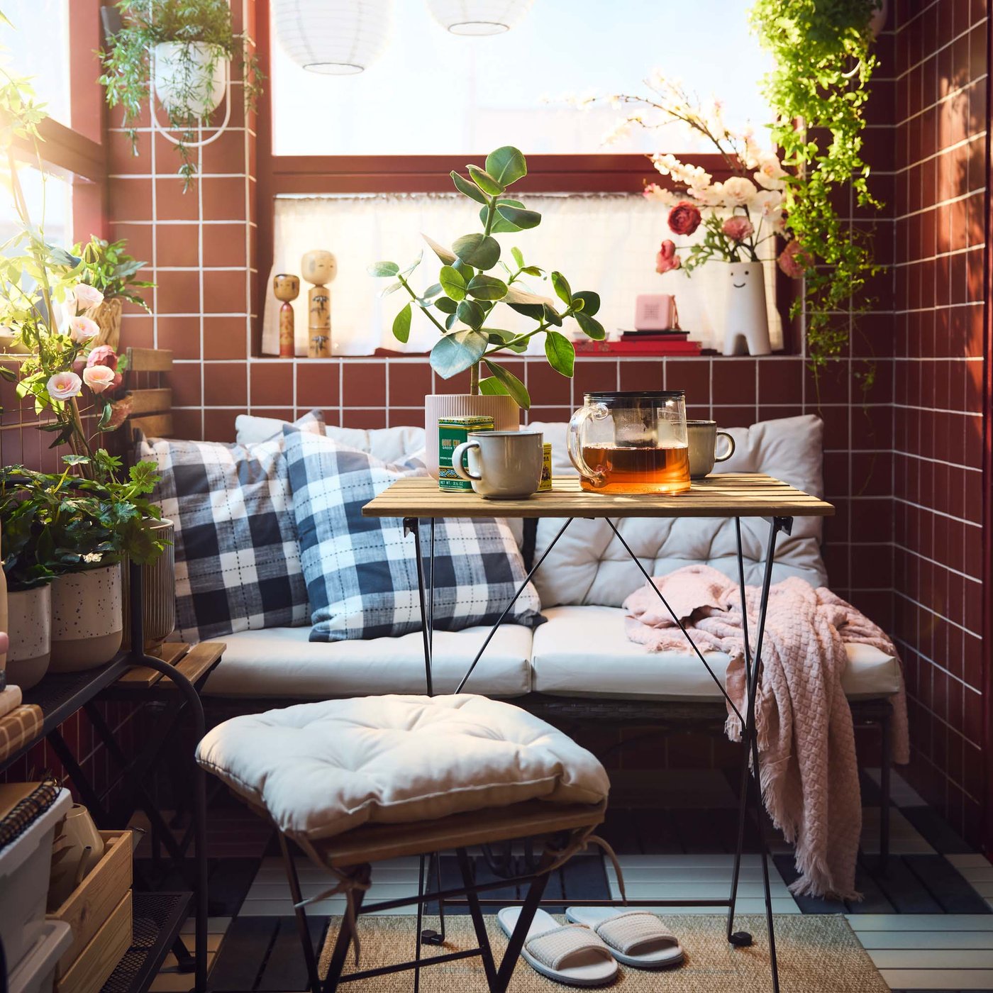 Outdoor seating with cushions next to a fold-up table with tea creates a cosy corner on a terrace.