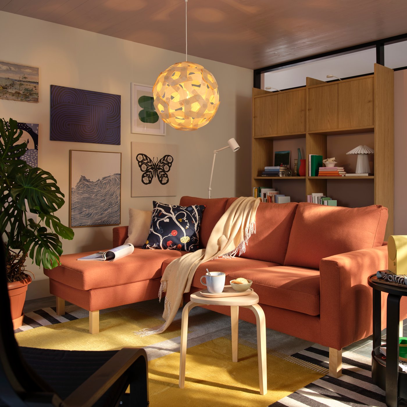 An orange L-shaped sofa in a white living room with a gallery wall and wood open and closed storage.