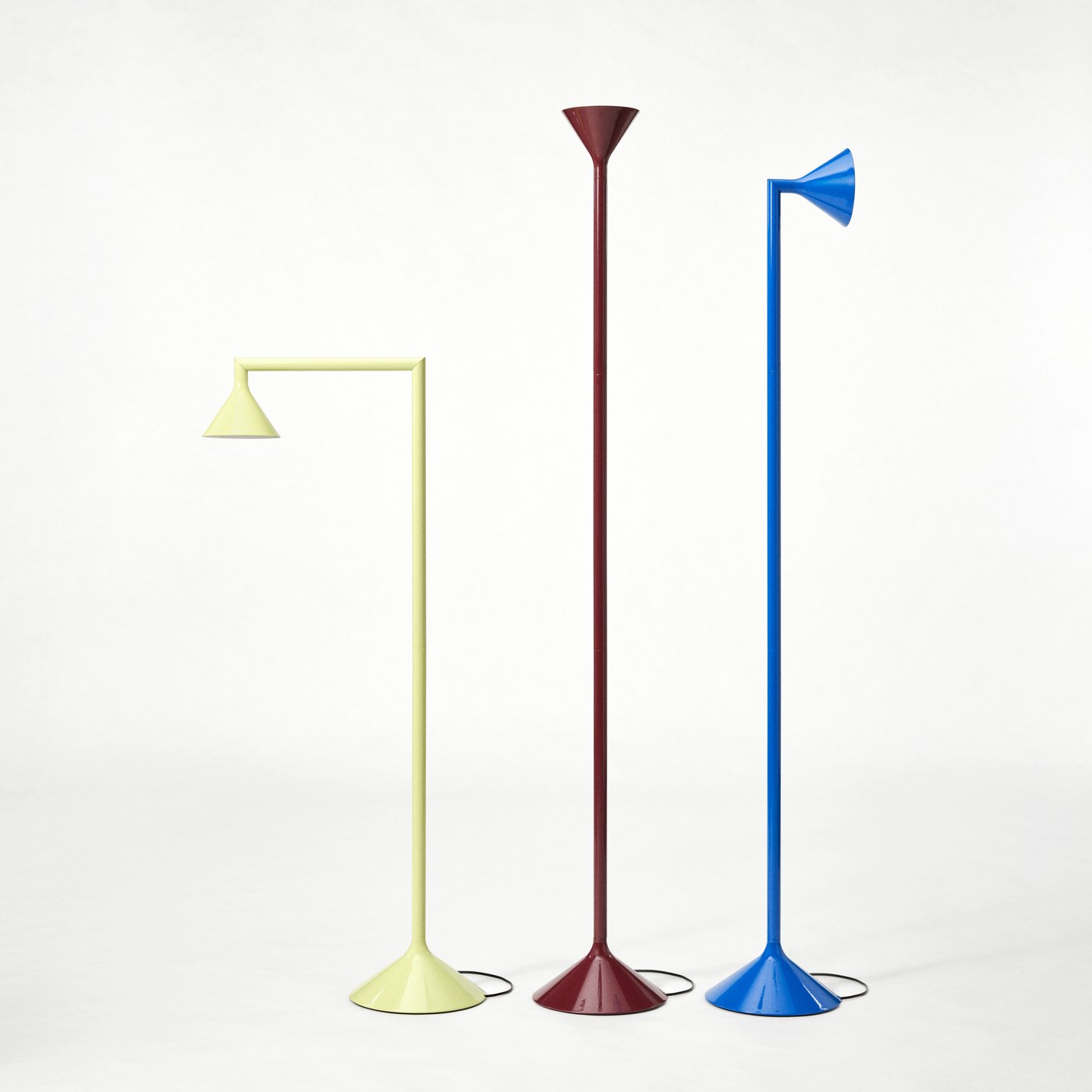 Three floor lamps in pale yellow, burgundy, and blue standing upright in a row against a white background.