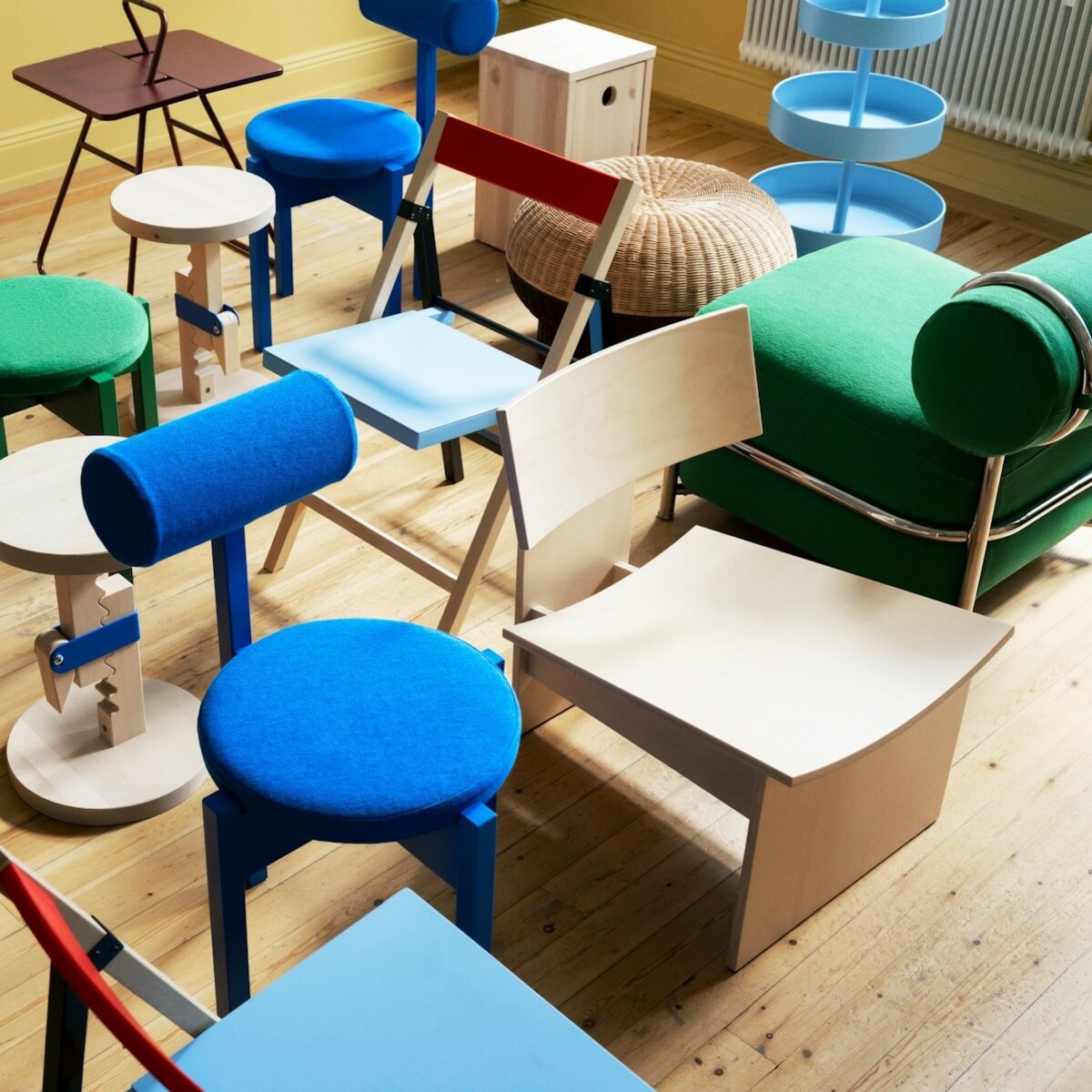 An overhead view of multiple IKEA PS 2026 pieces displayed together on a wooden floor, including stools, chairs, tables and storage.