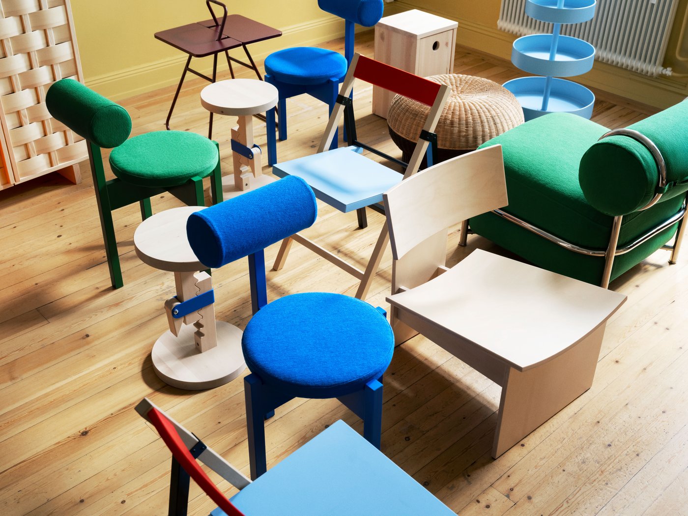 Assortment of chairs and small tables in various colors and materials arranged on a wooden floor, including blue, green, and natural wood finishes.