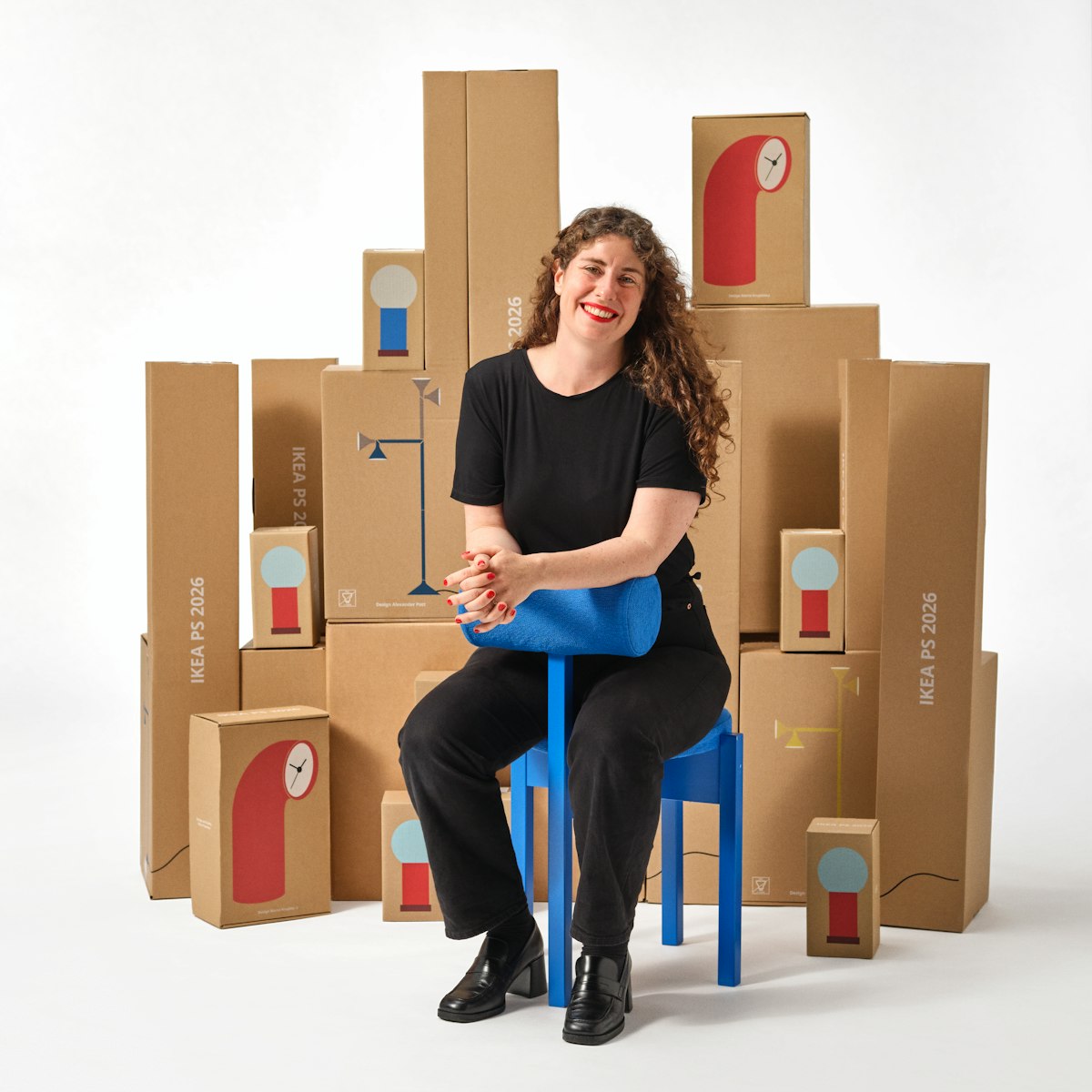 Maria O'Brian sits on a blue stool with packaging from the IKEA PS 2026 collection behind her. She smiles at the camera.