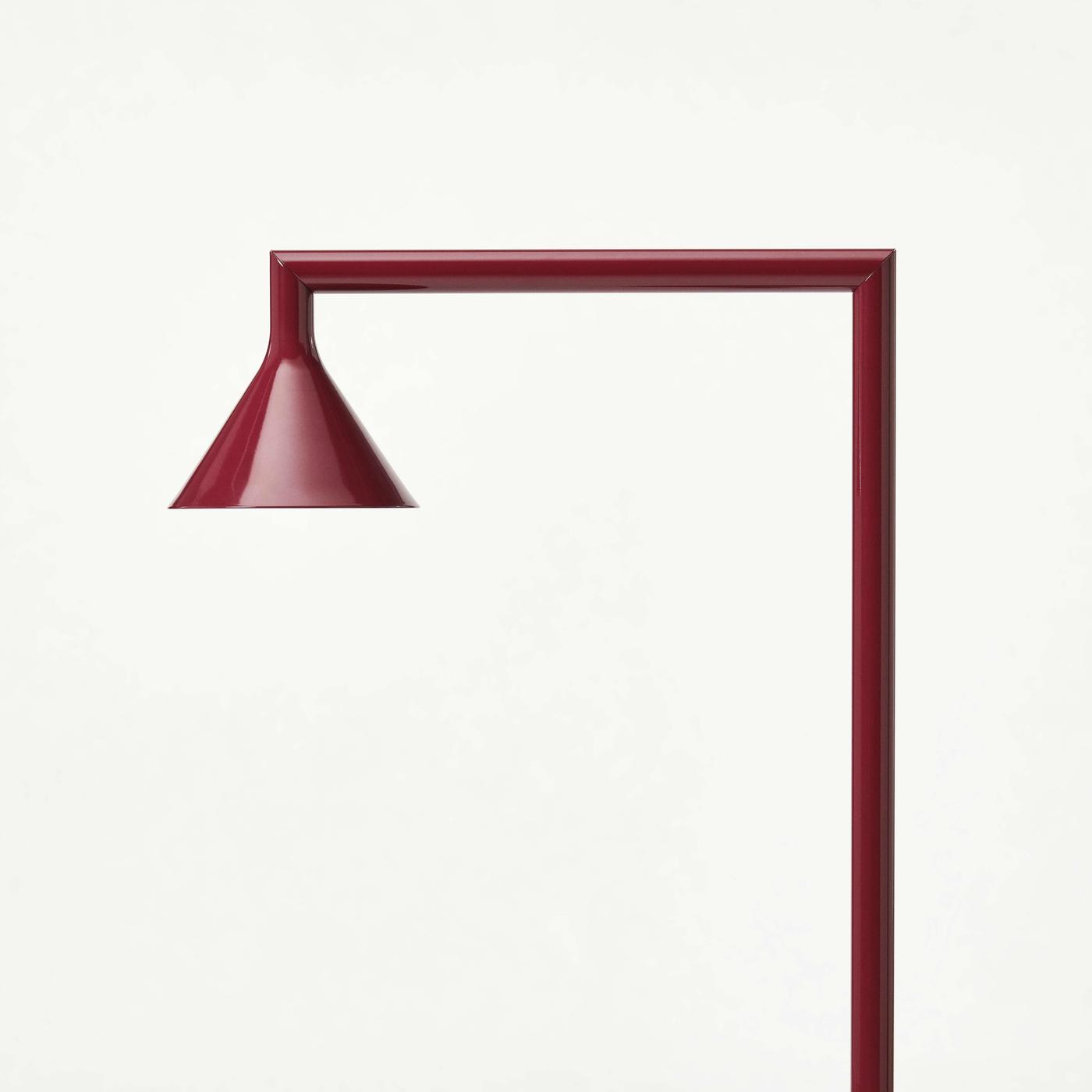 A red IKEA PS 2026 floor uplighter with a bent stand, on a light grey background.