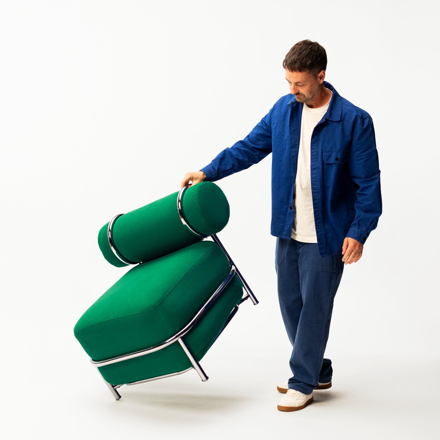Designer Mikael Axelsson in a blue jacket guiding a green air-filled and upholstered chair tilted forward against a white background.