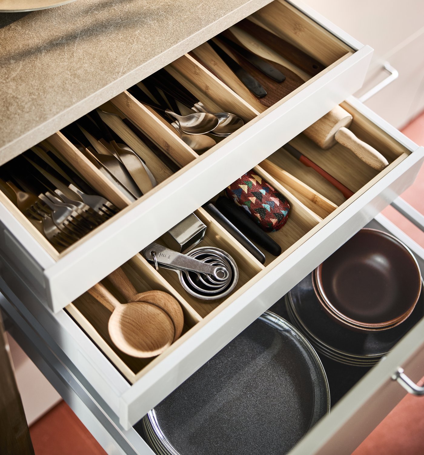Opened kitchen drawers with wooden utensils, cutlery, measuring cups and other assorted cooking tools, neatly organised by a bamboo cutlery tray.