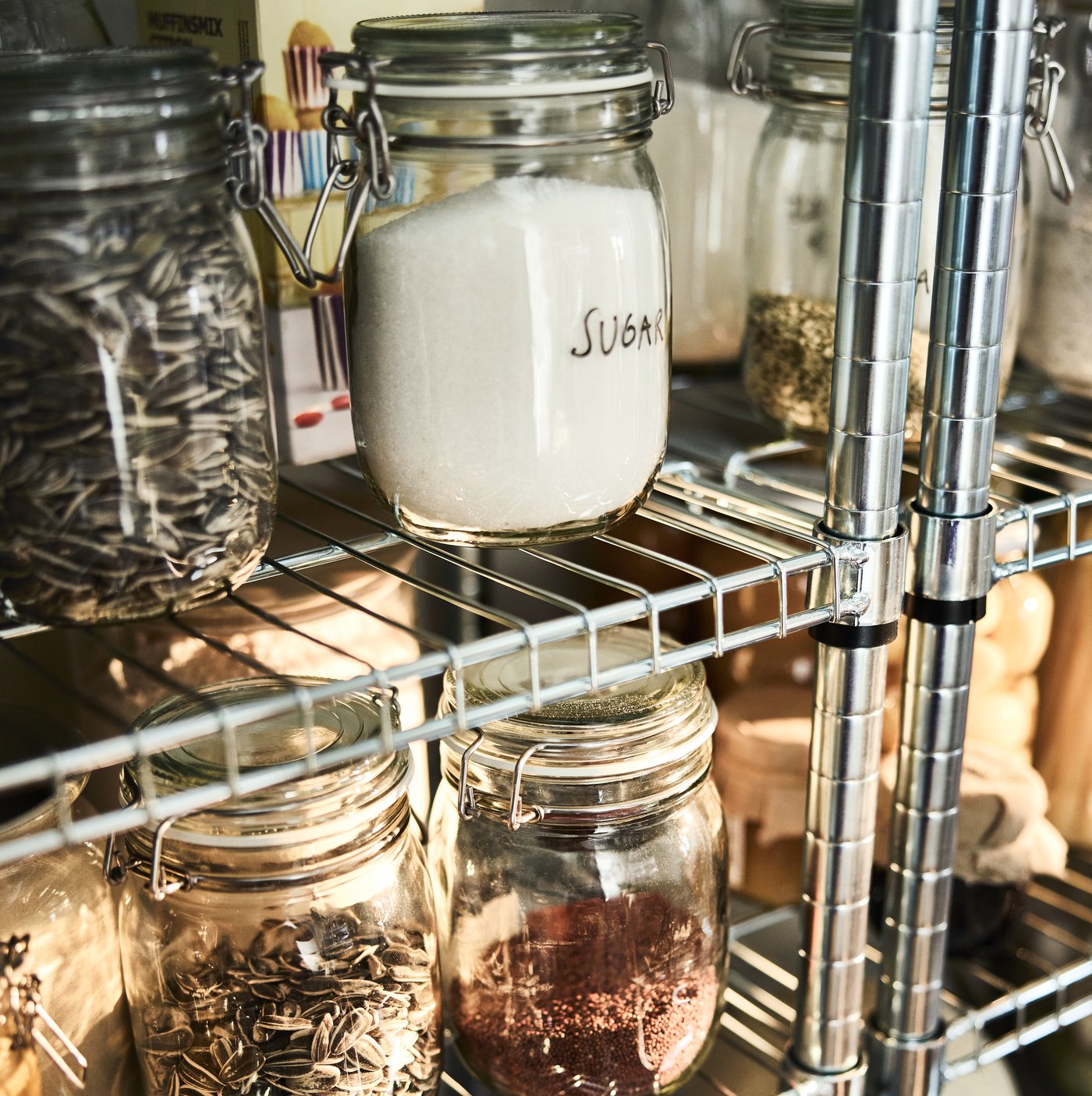 An OMAR metal shelving unit with glass KORKEN jars with labels ingredients written on them, in a neatly organised pantry space.