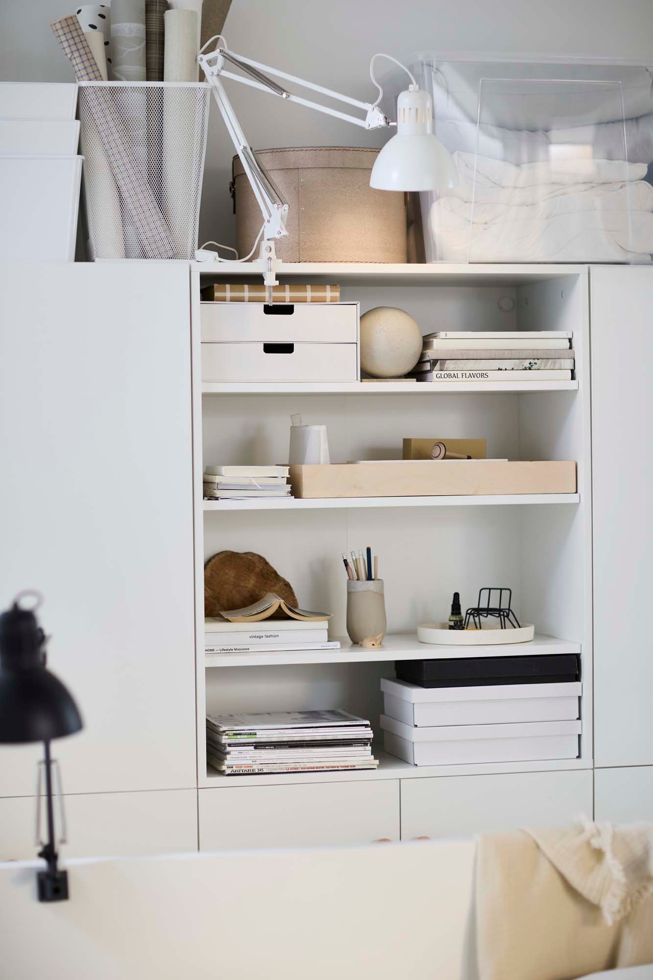 White shelving filled with stationary and smaller storage containers surrounded by closed storage. 