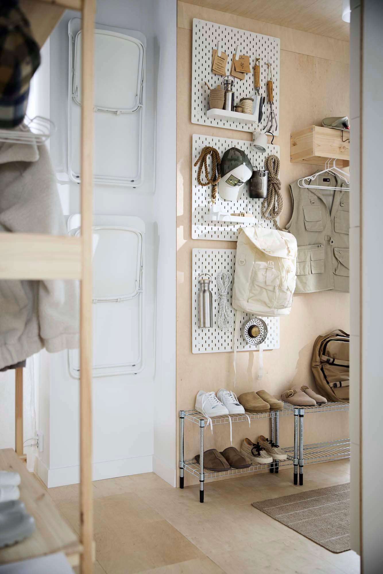 A light wood hallway with white pegboards, a metal shoe rack and wooden coat rack.