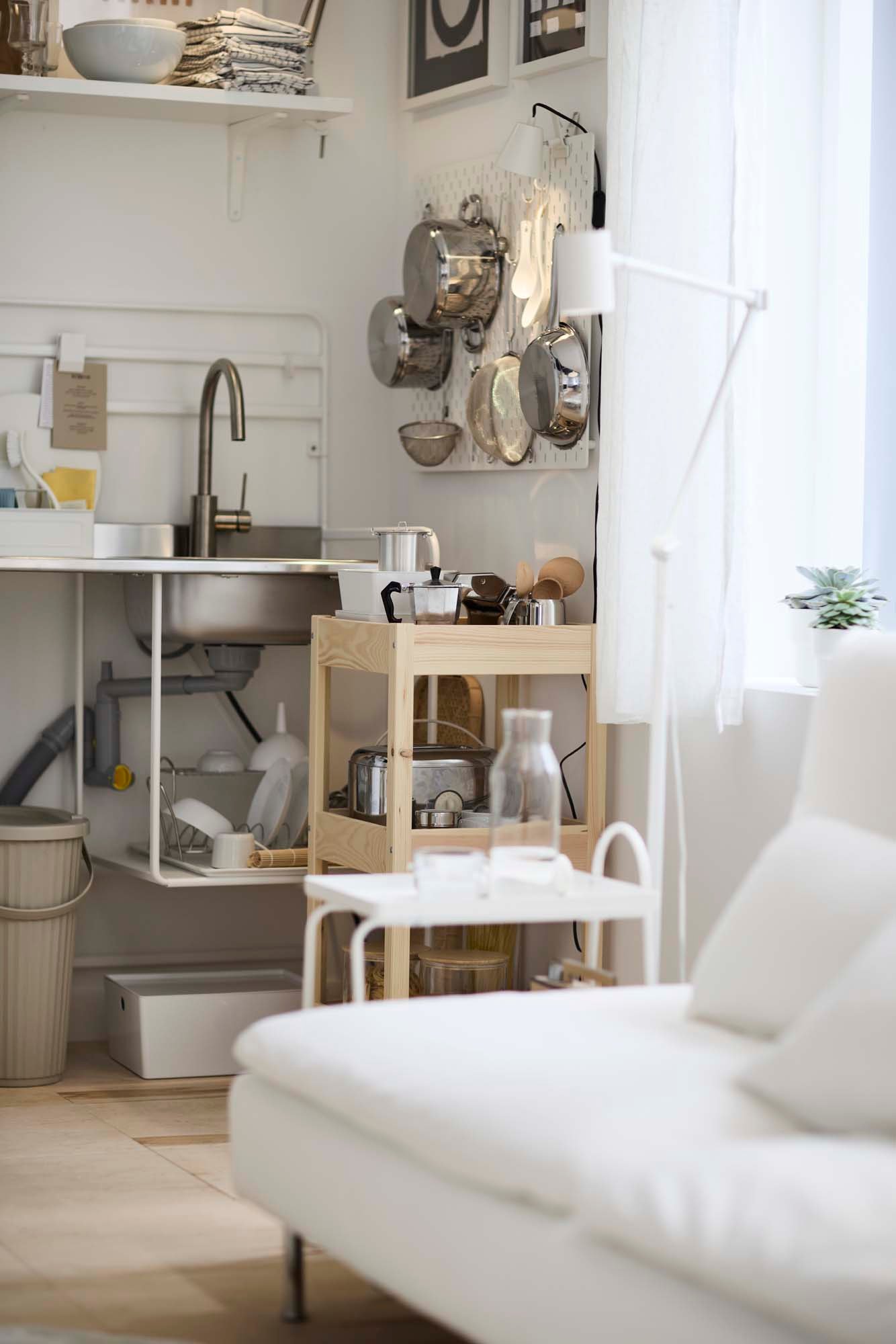 Pots and pans hang on a peg board over a wooden trolley in the corner of an open-plan kitchen and living room area.