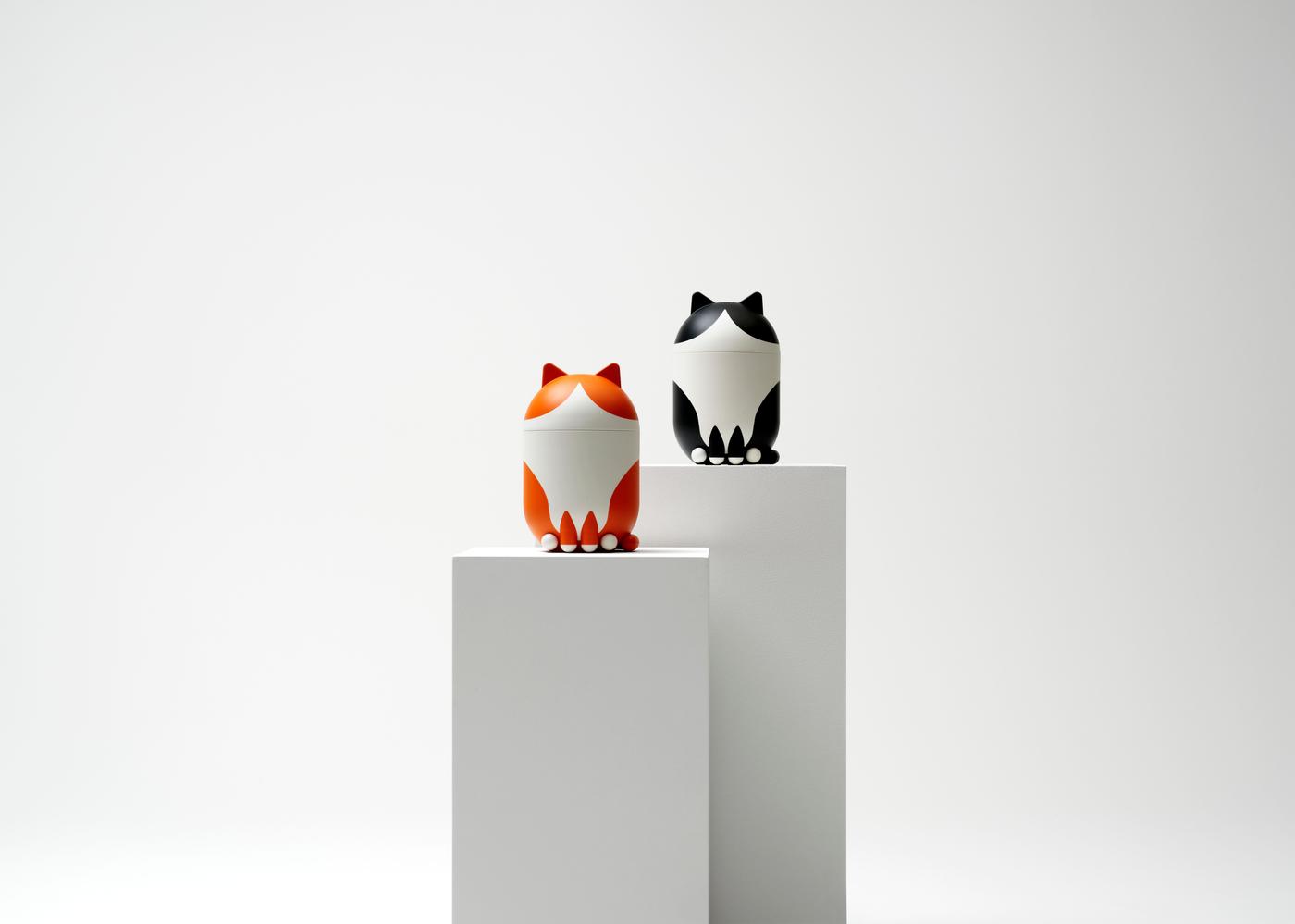 Two cat-shaped decorative storage jars standing on a white pedestal against a white background.