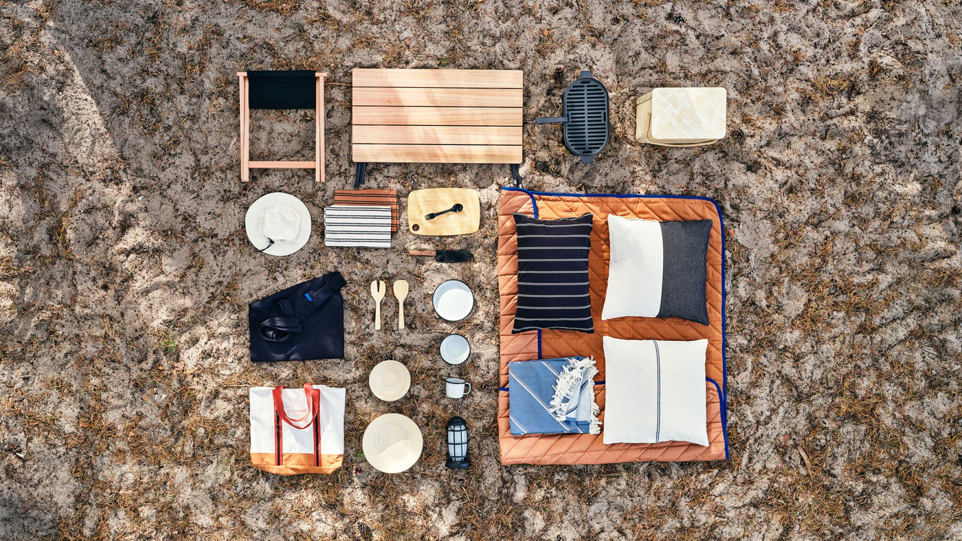 Overhead view of items from this collection on gravel, including plates, cutlery, cups, textiles and storage containers in neutral tones.