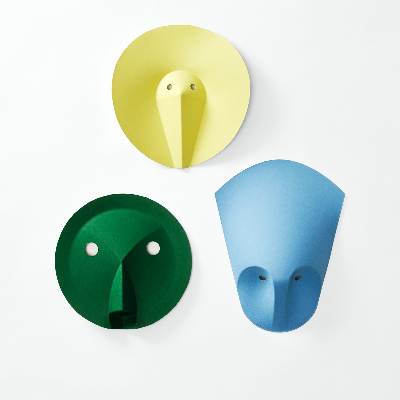 Close-up view of several wall hooks in green, yellow, and blue, showing their sculptural, face-like forms.