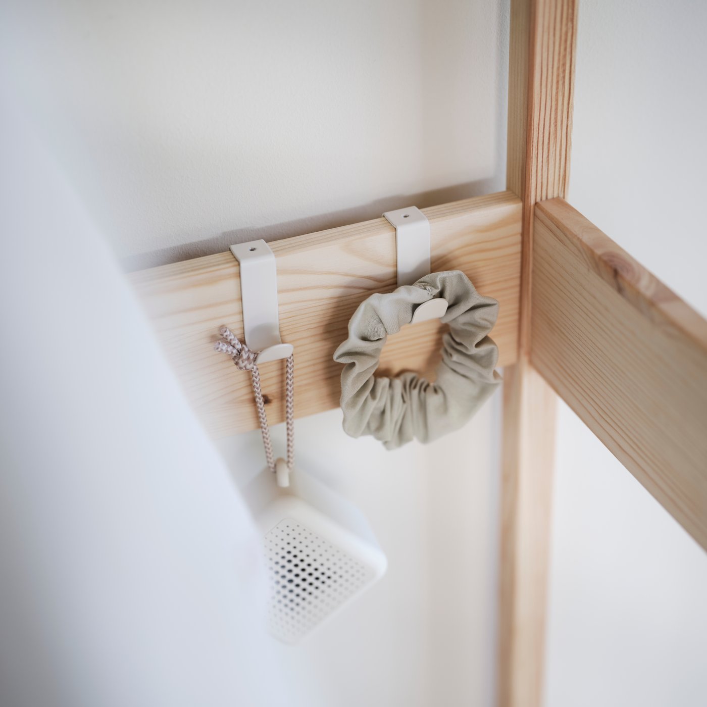 A close-up of the inside of the KRONÖREN open wardrobe with two white clips holding a speaker and hair scrunchy.