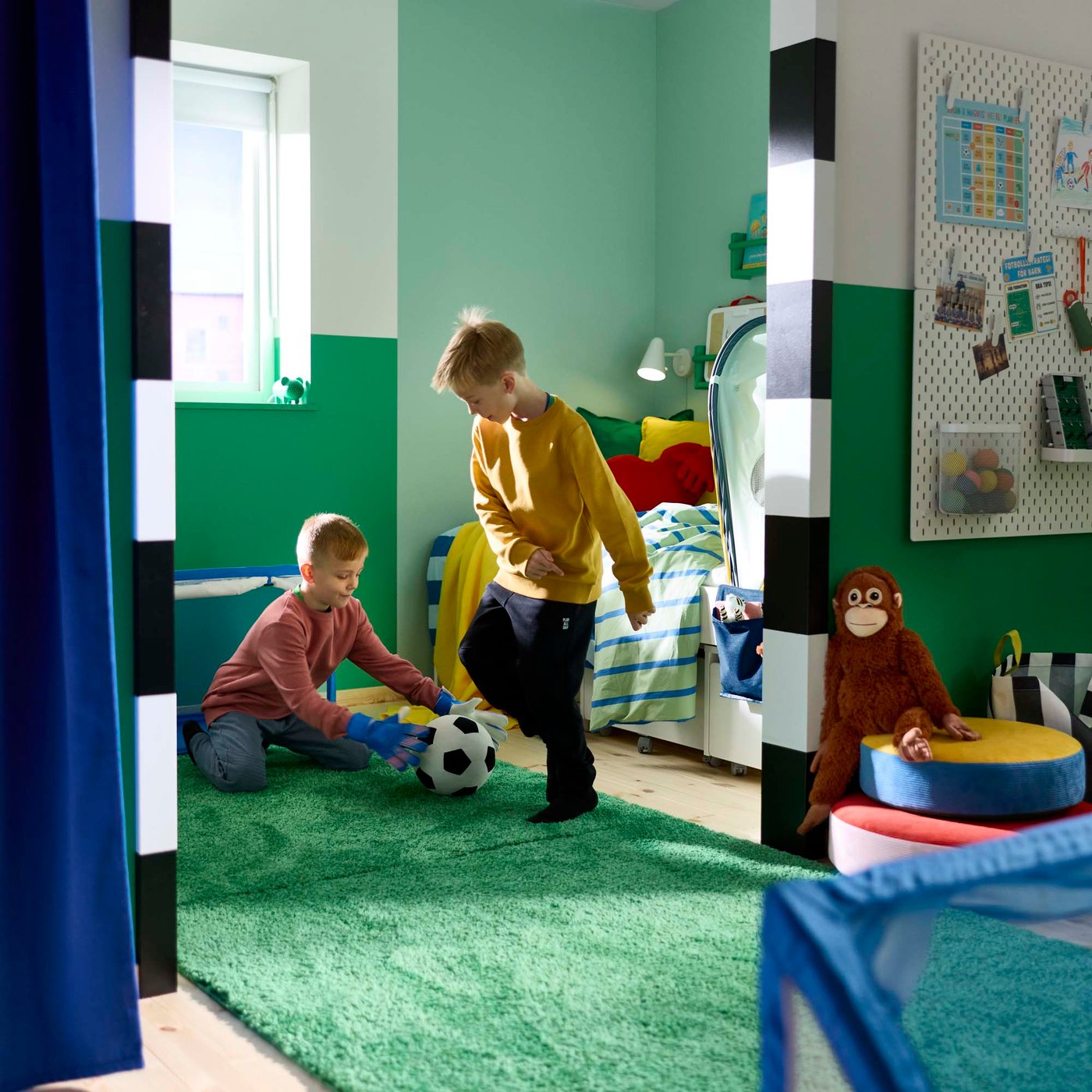 Two children playing football on a green rug in a football-themed bedroom.