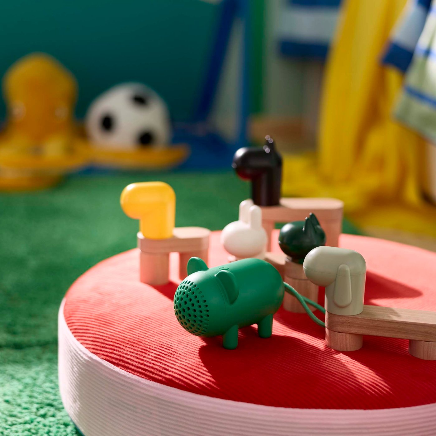 A series of wooden figurine building blocks and a bluetooth speaker on a red and pink floor cushion.