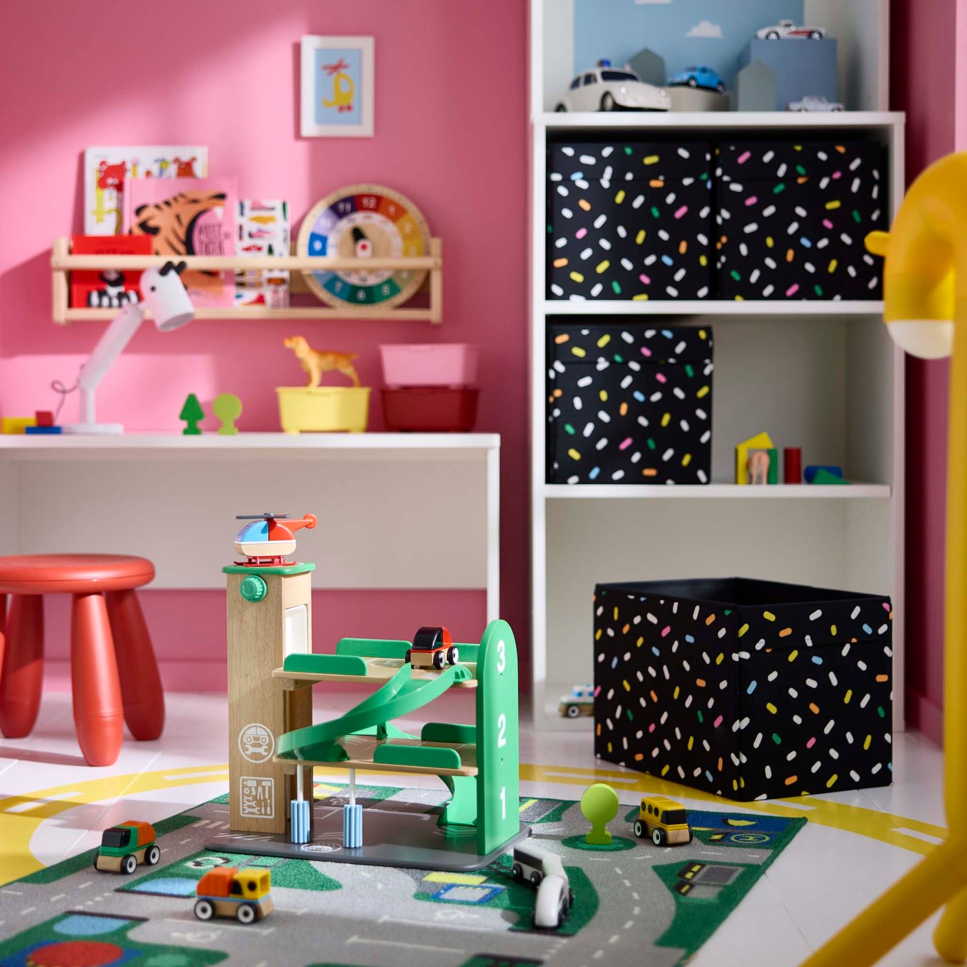 A green toy garage on the floor of a pink and white children's bedroom.