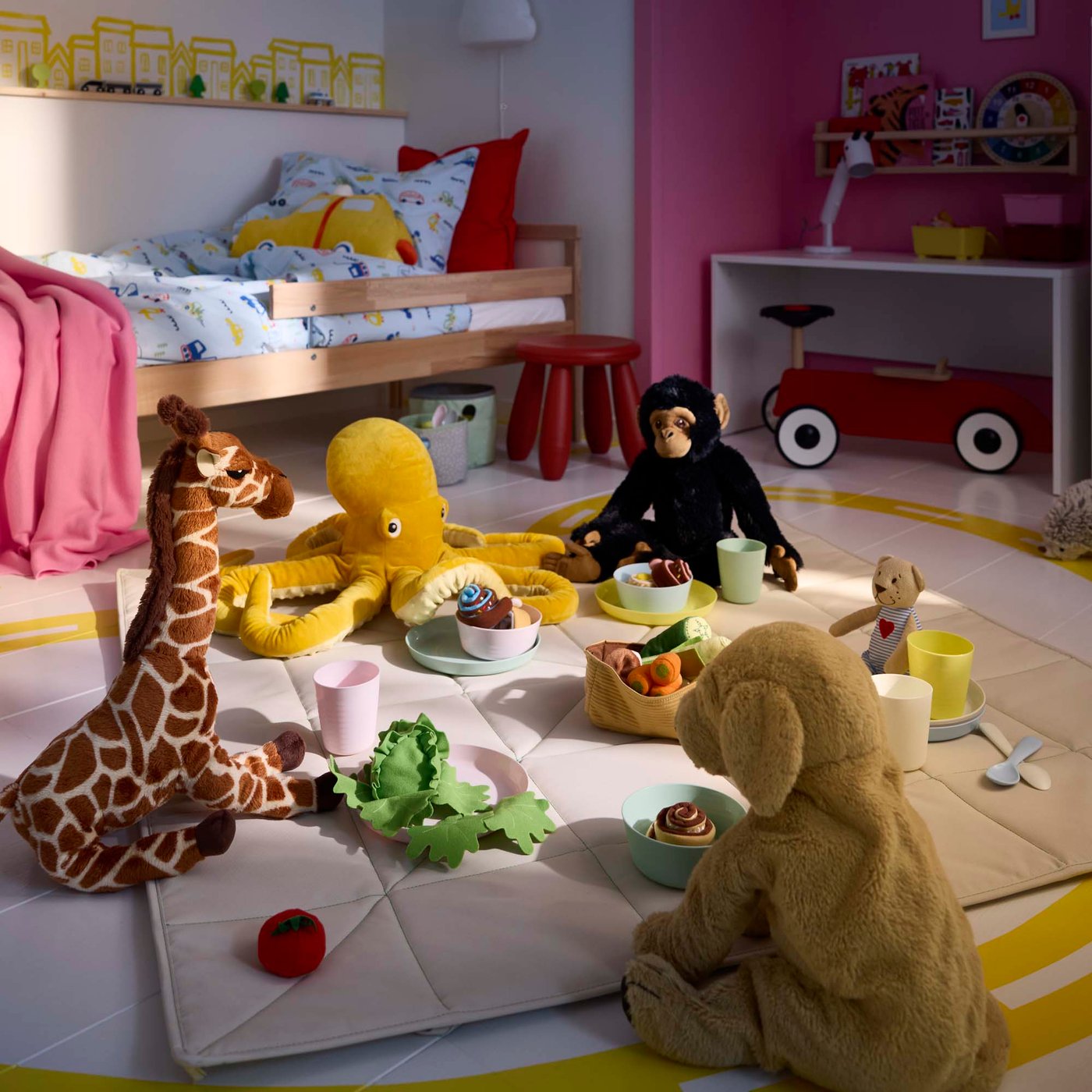 A group of soft toys animals enjoying a picnic on a blanket in a children's bedroom.