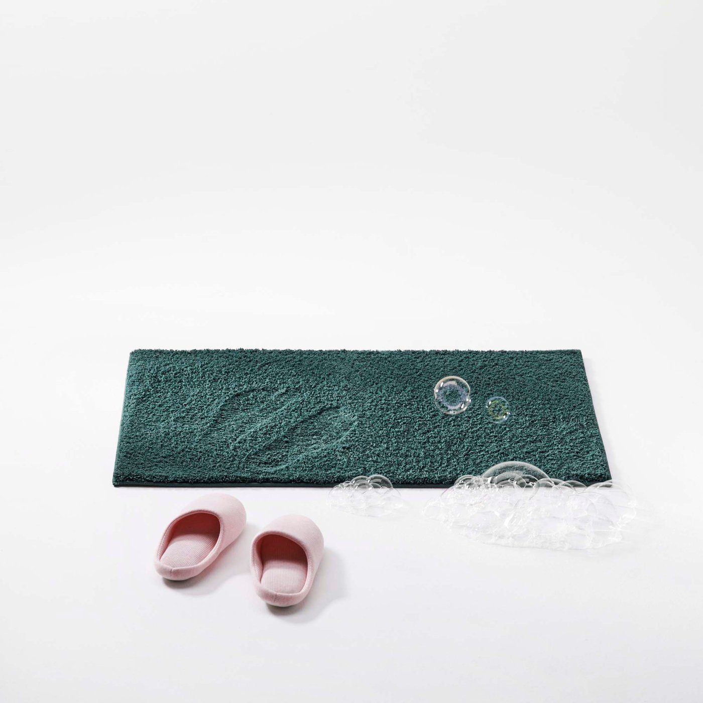Pink slippers in front of a dark green bath mat.