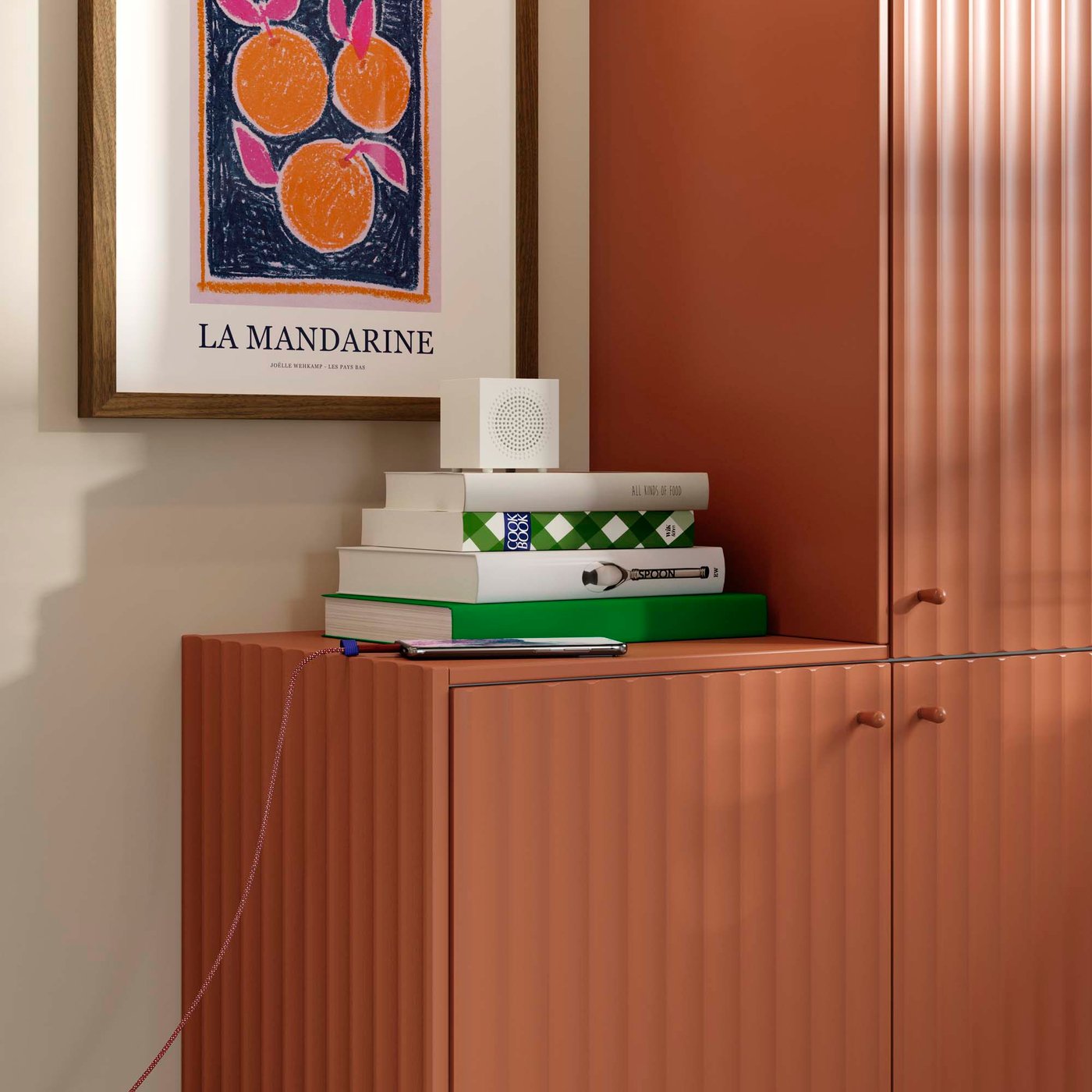 A Bluetooth speaker rests on a pile of books atop red-brown kitchen fronts with a wave pattern.