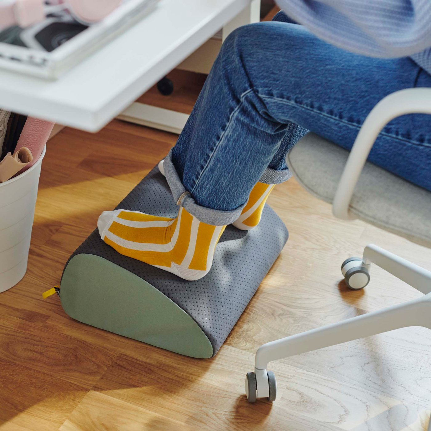 A person sits at a desk with their feet on an ergonomic footrest.