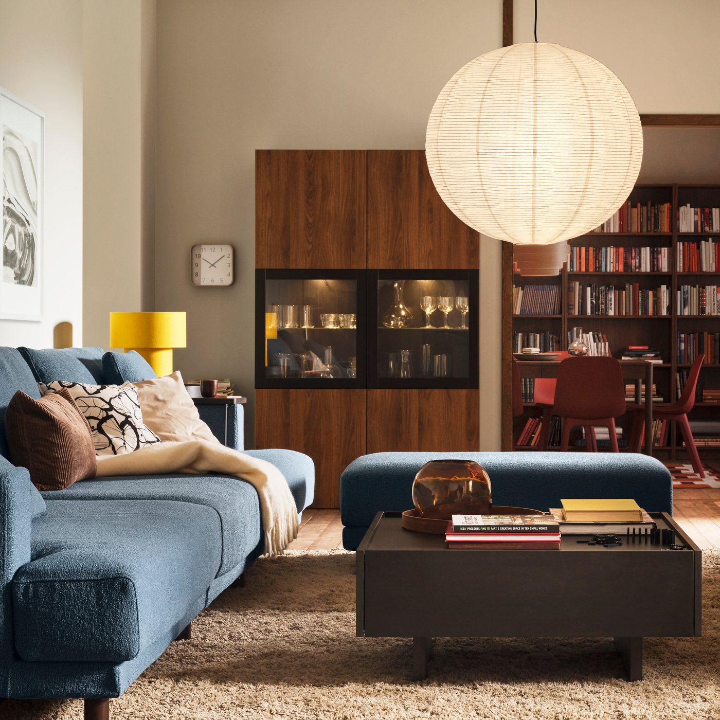 A blue sofa and pouffe and a black coffee table in front of a dining area with dark wood open and closed storage behind.