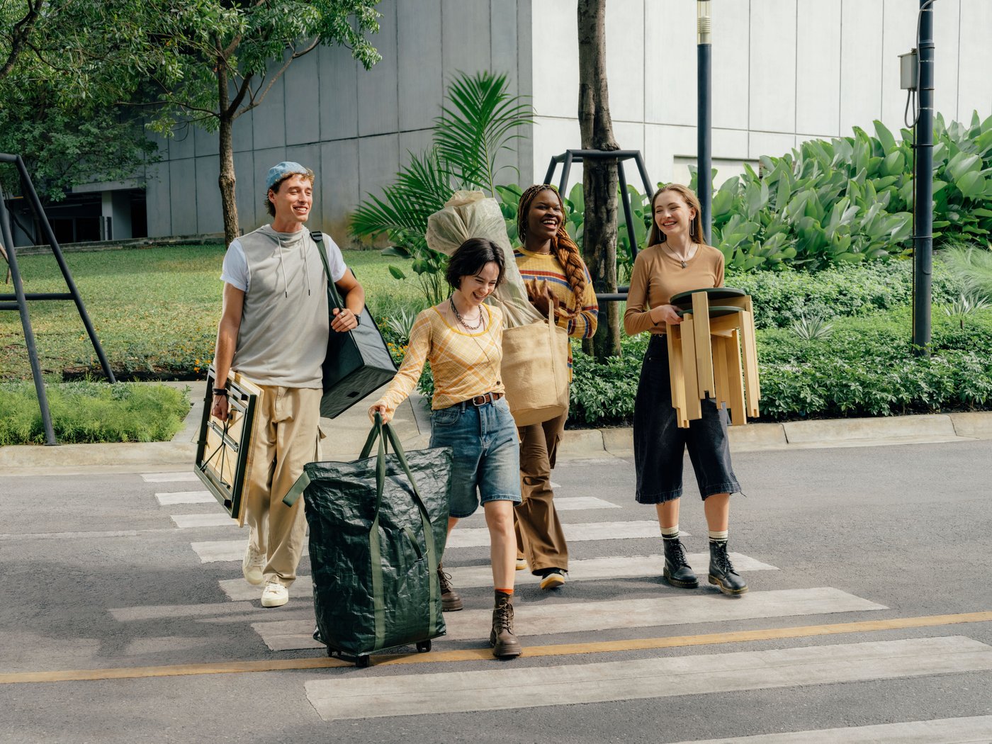 A group of four young adults crossing a road while carrying products from the KOMPISHÄNG collection.