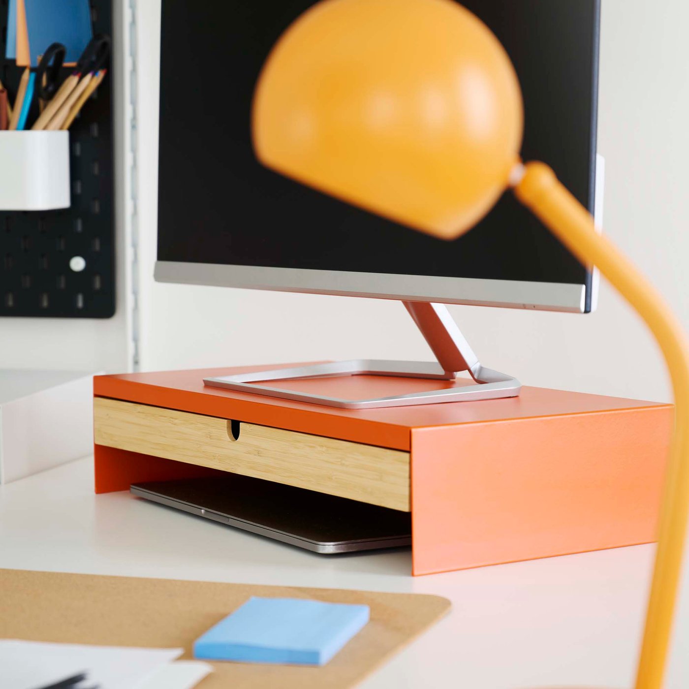 Close-up of an orange retro style lamp next to an orange monitor stand on a white desk.