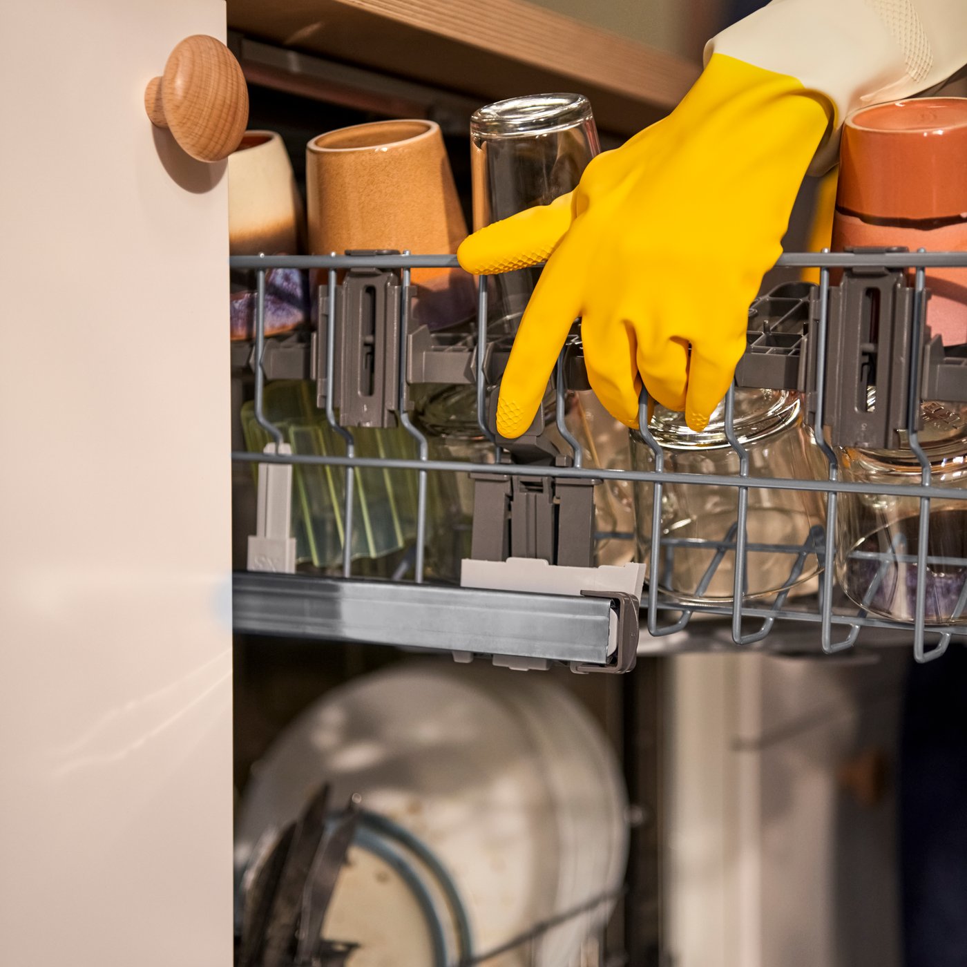 A person wearing a yellow rubber glove holding onto the top shelf of a dishwasher.